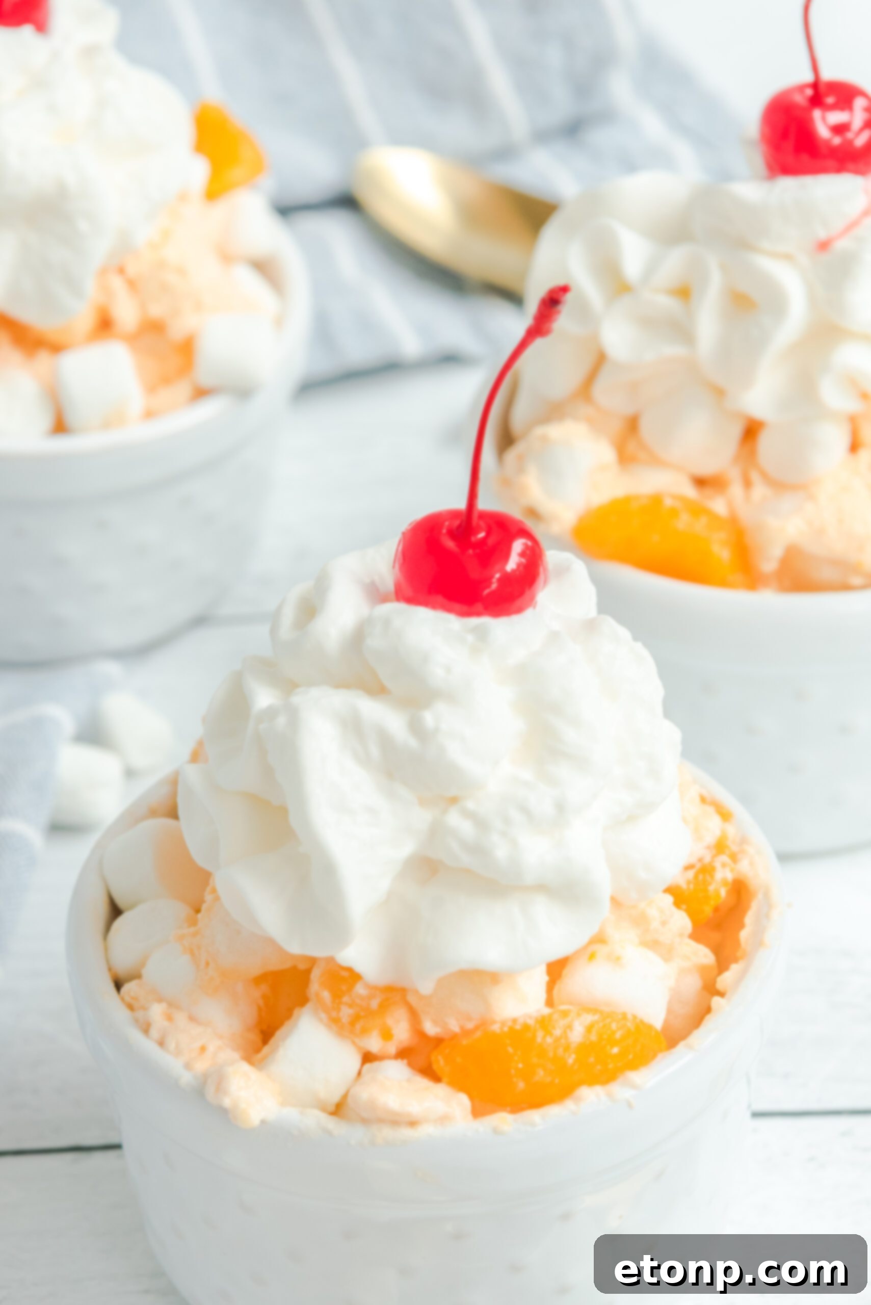 A close-up shot of Orange Creamsicle Salad in a white bowl, topped with a delicate swirl of whipped cream.