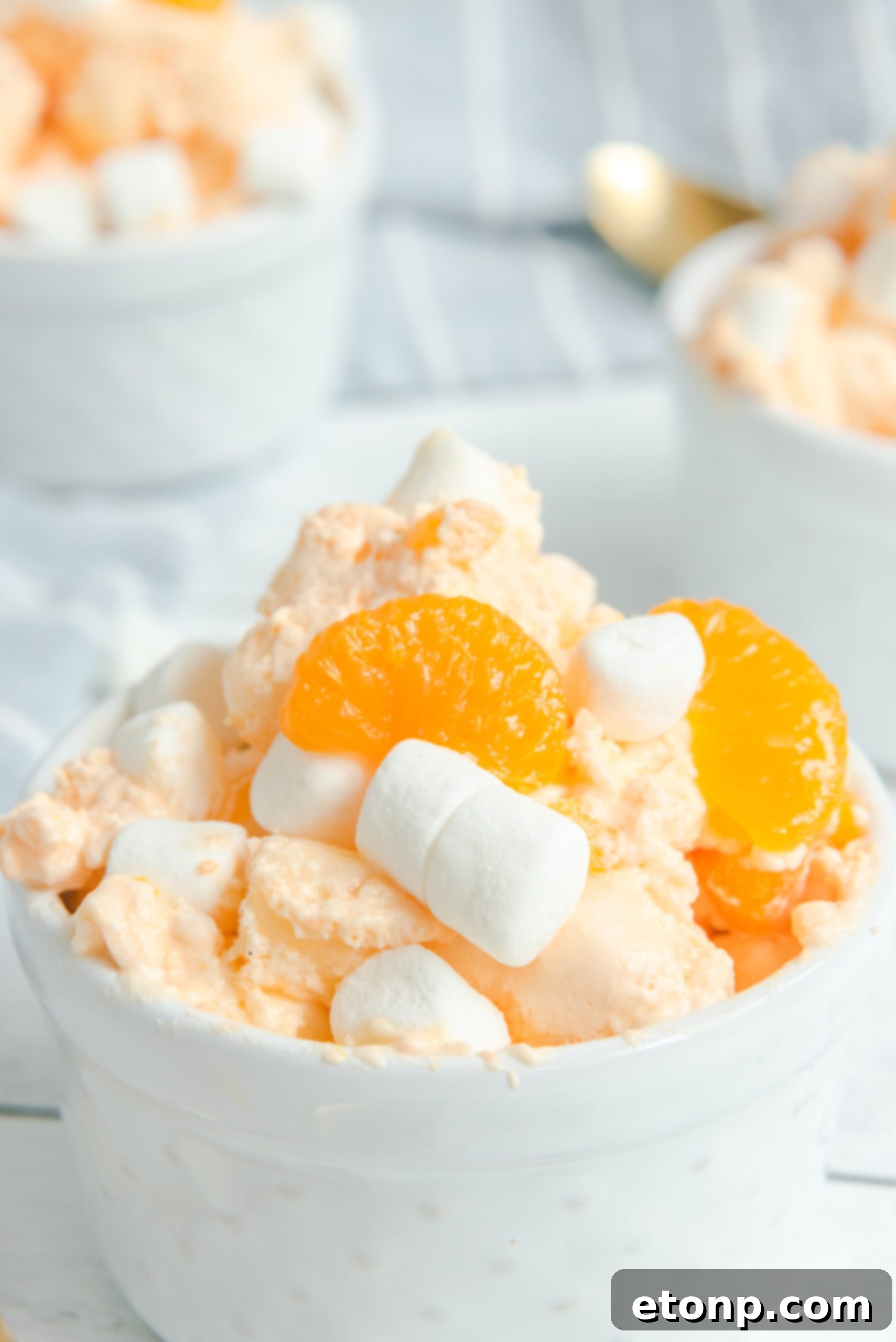A close-up view of Orange Creamsicle Salad in a white bowl, garnished with fluffy marshmallows and juicy mandarin orange slices.