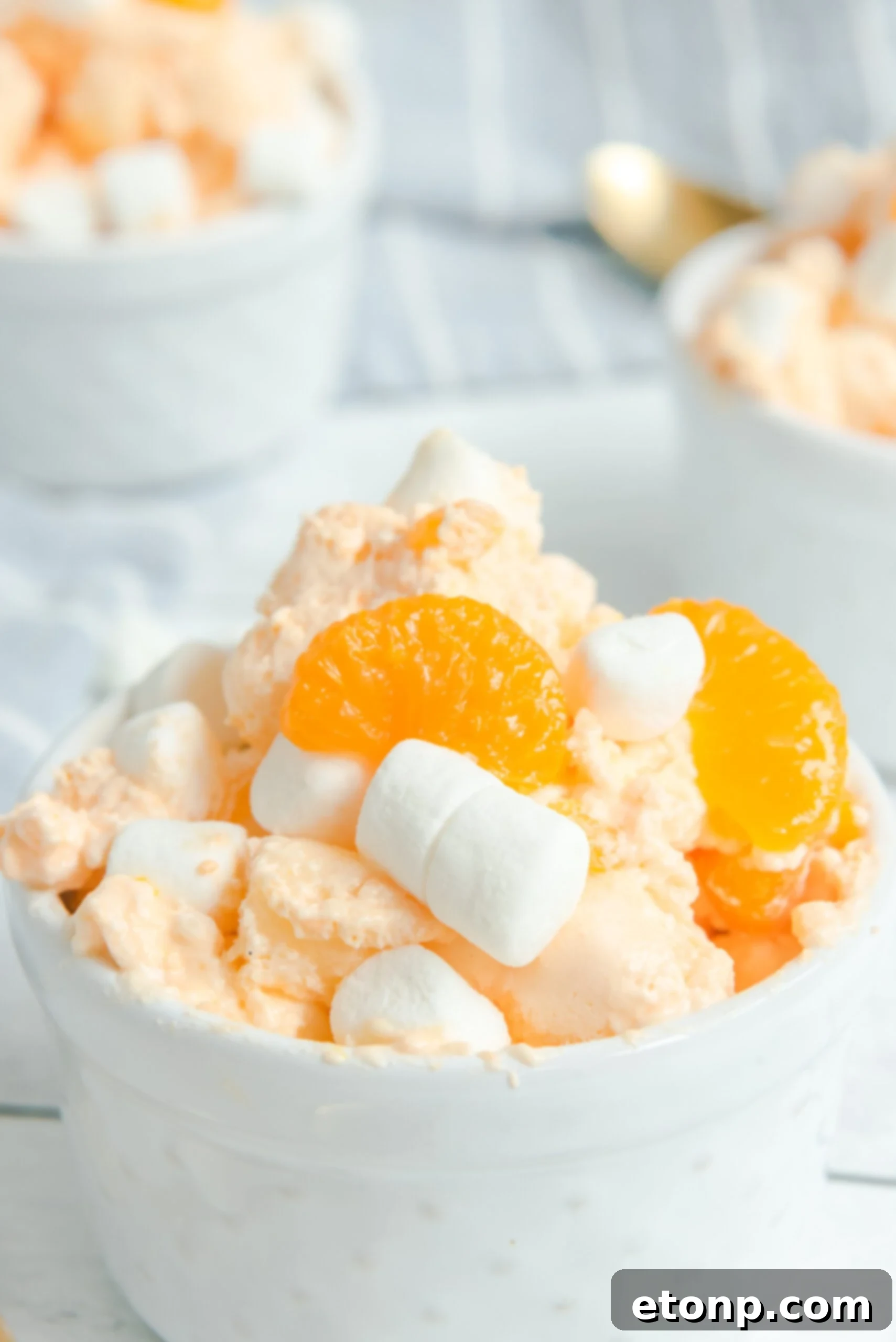 A close-up shot of Orange Creamsicle Salad in a white bowl, showcasing its fluffy texture and toppings of marshmallows and mandarin oranges.