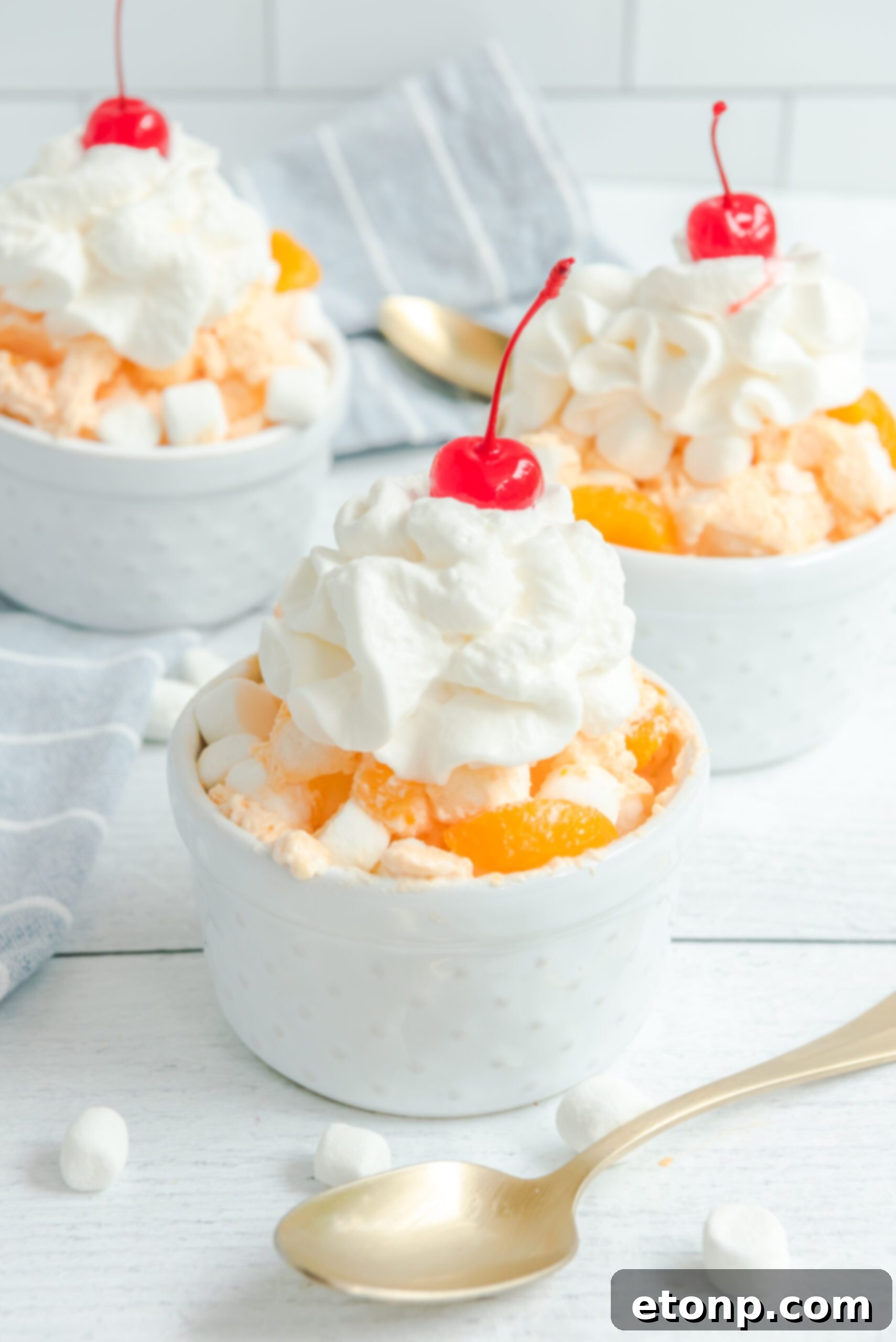 Three white bowls of Orange Creamsicle Salad, each adorned with whipped cream and a cherry, arranged neatly.