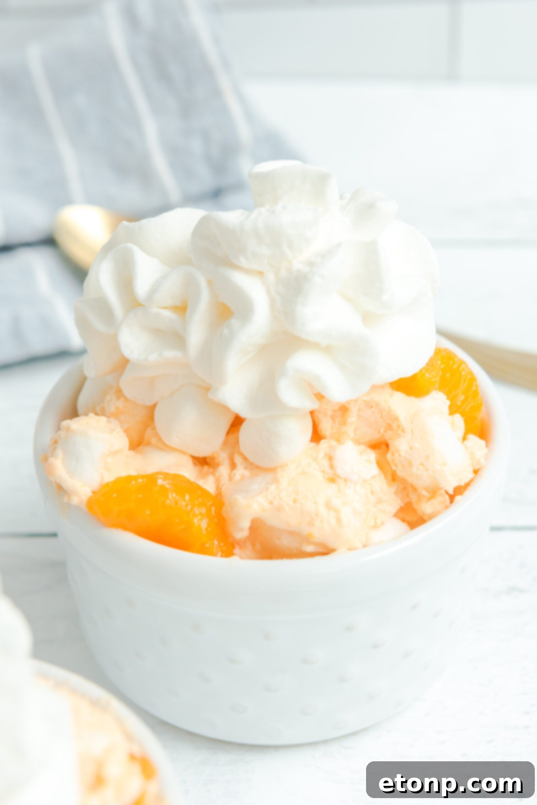 Orange Creamsicle Salad in a white bowl, lavishly topped with whipped cream and colorful mandarin orange segments.