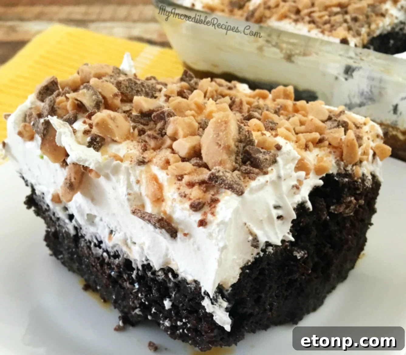 Another enticing close-up photograph of the caramel-drenched chocolate poke cake, layered with whipped cream and crunchy Heath bar pieces.