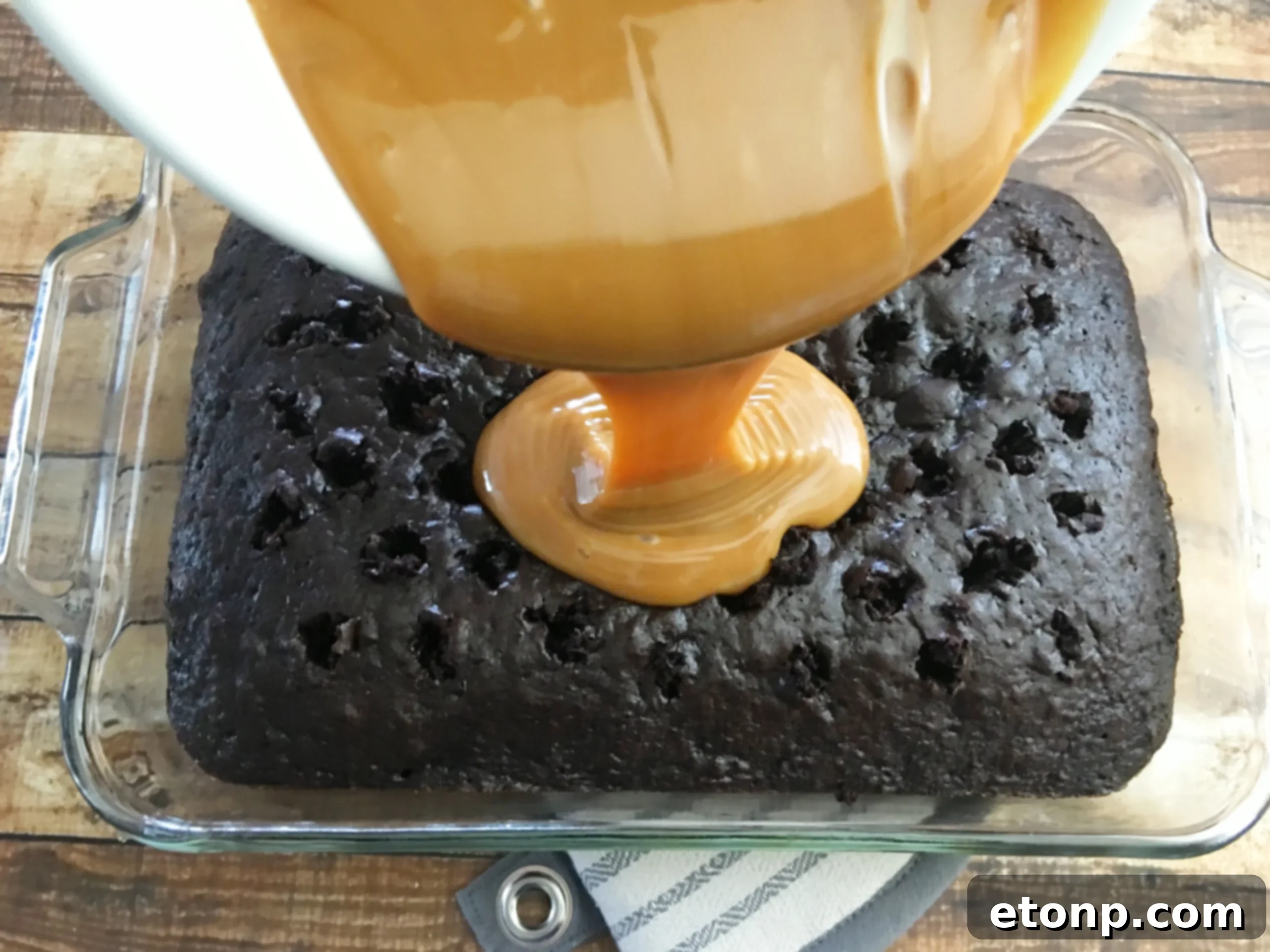 The chocolate cake after soaking up the caramel and condensed milk, appearing moist and ready for the next layer of whipped topping.