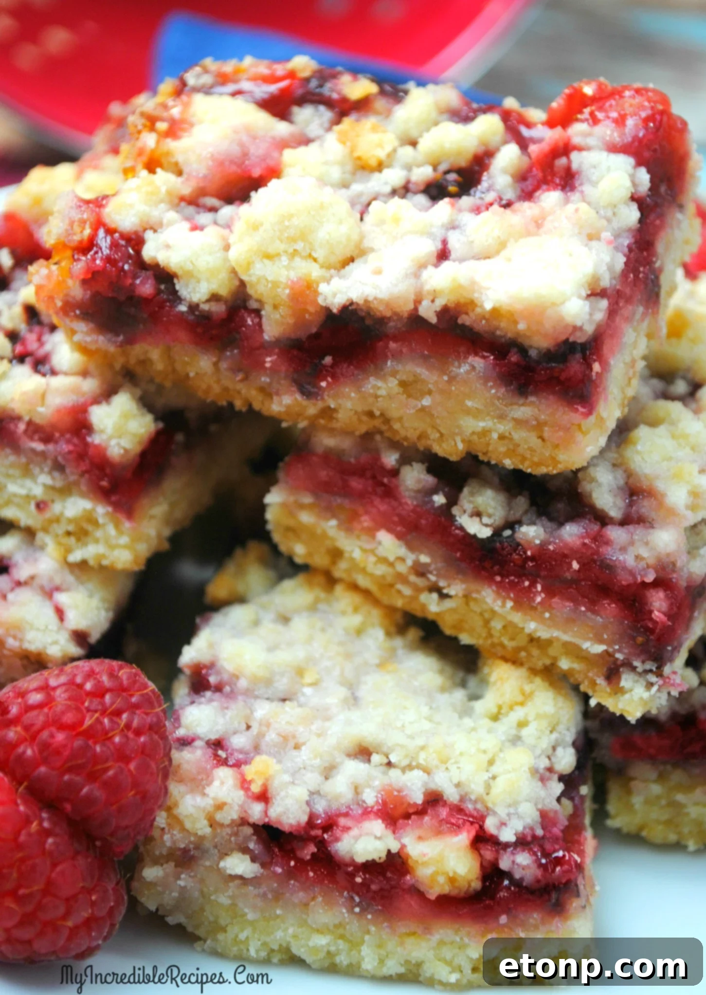Stacked Raspberry Crumble Bars on a white plate, garnished with a few fresh raspberries.