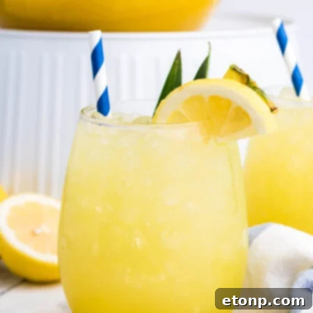 Pineapple Lemonade in a clear glass, a close up with ice and a lemon wedge