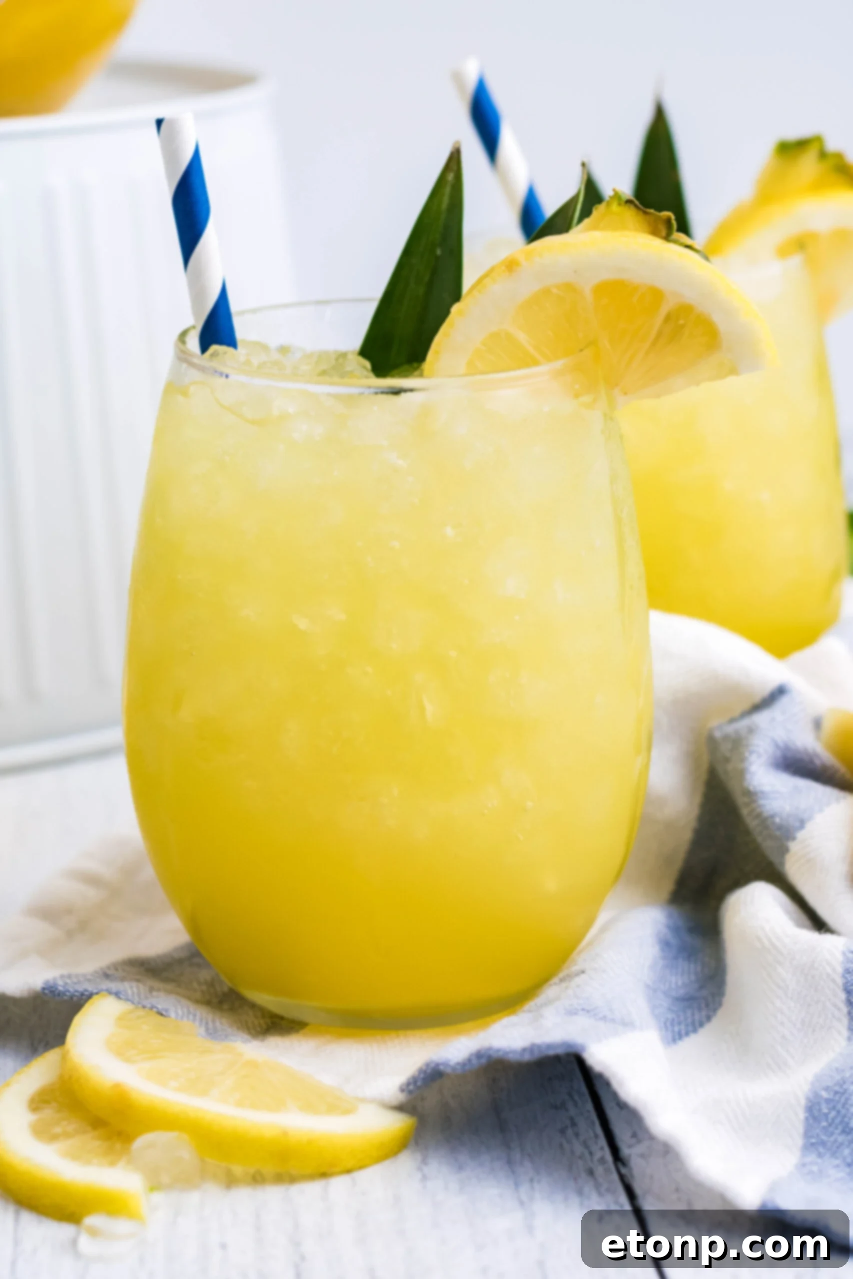 Pineapple Lemonade in a clear glass with ice, garnished with a fresh lemon slice and a vibrant blue straw