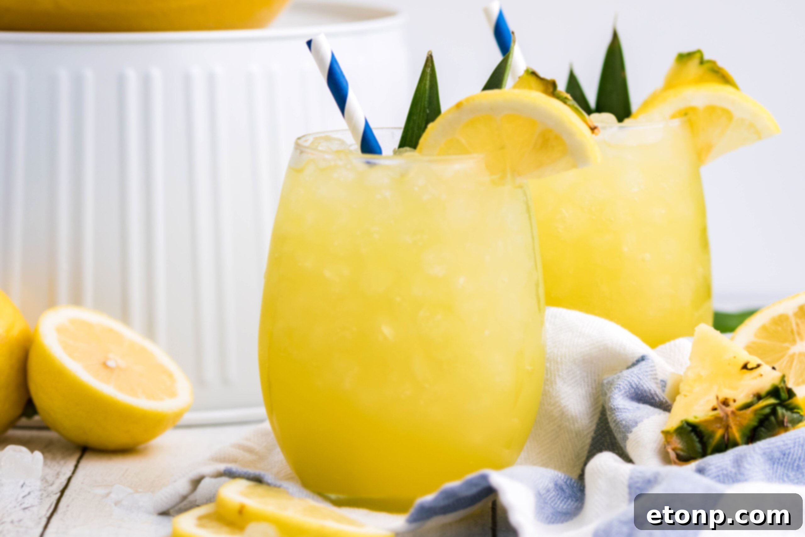 Pineapple Lemonade in a clear glass with ice and a blue striped straw, garnished with a fresh lemon slice