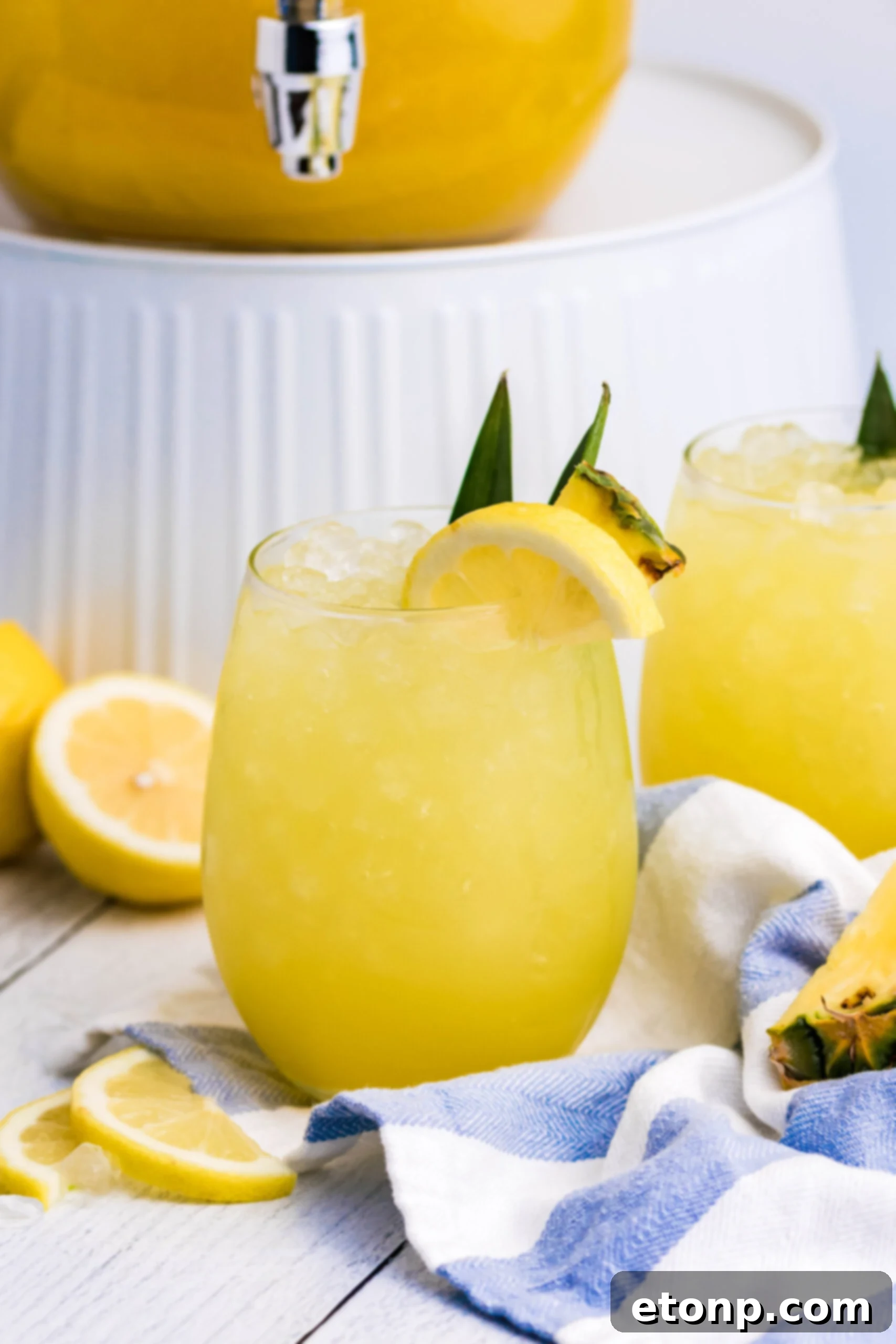 Pineapple Lemonade in a clear glass with ice and a blue straw on a simple white wooden table