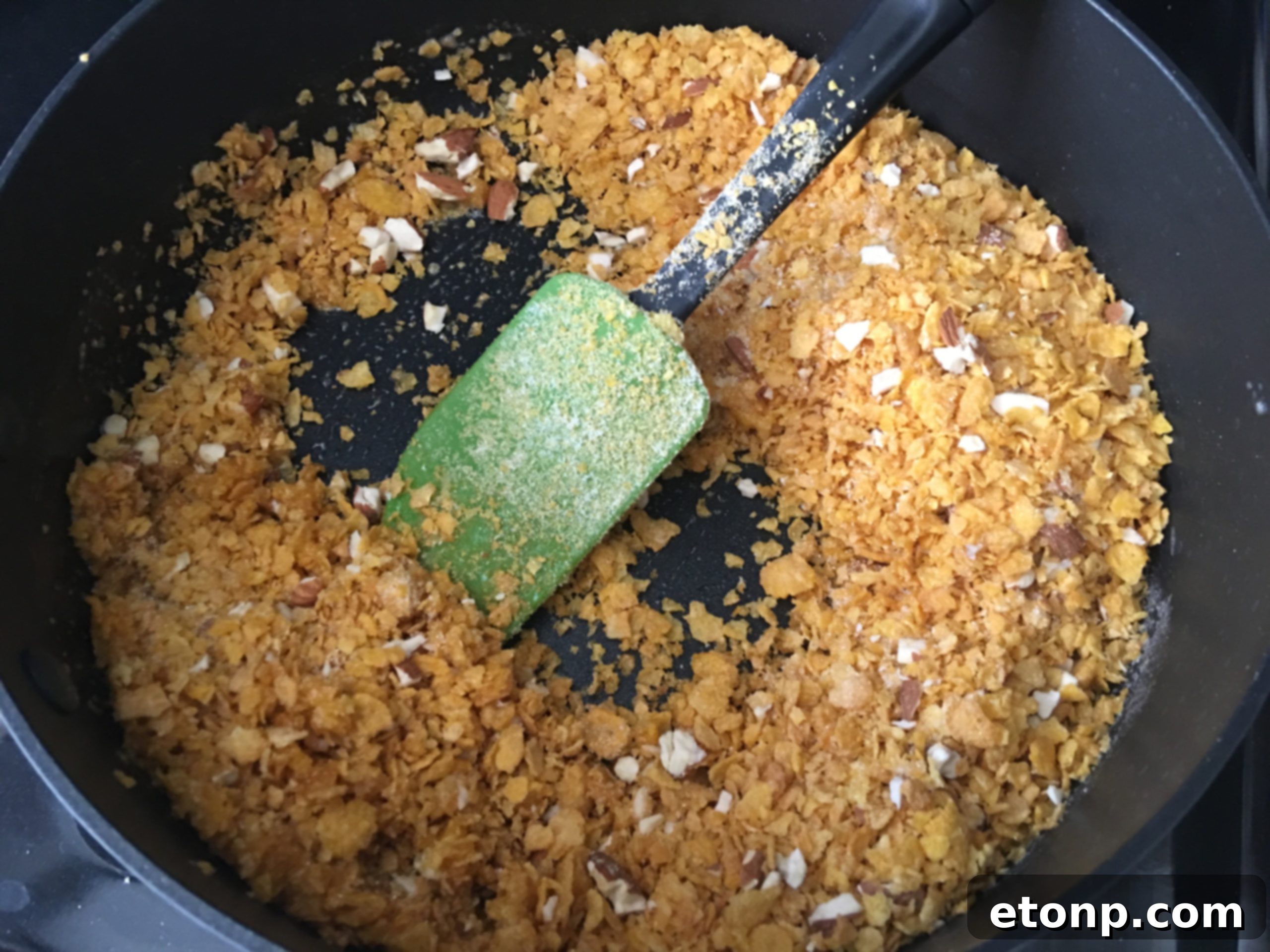 Close-up view of cornflakes, crushed nuts, and sugar toasting in melted butter in a skillet.
