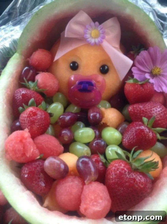 Creative fruit arrangement featuring a watermelon carved into a baby carriage, filled with various colorful fruits.