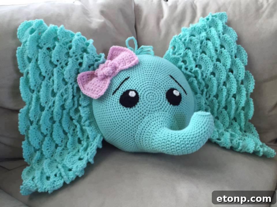 Adorable grey crocheted elephant-shaped pillow with big ears and a trunk, lying on a white surface.