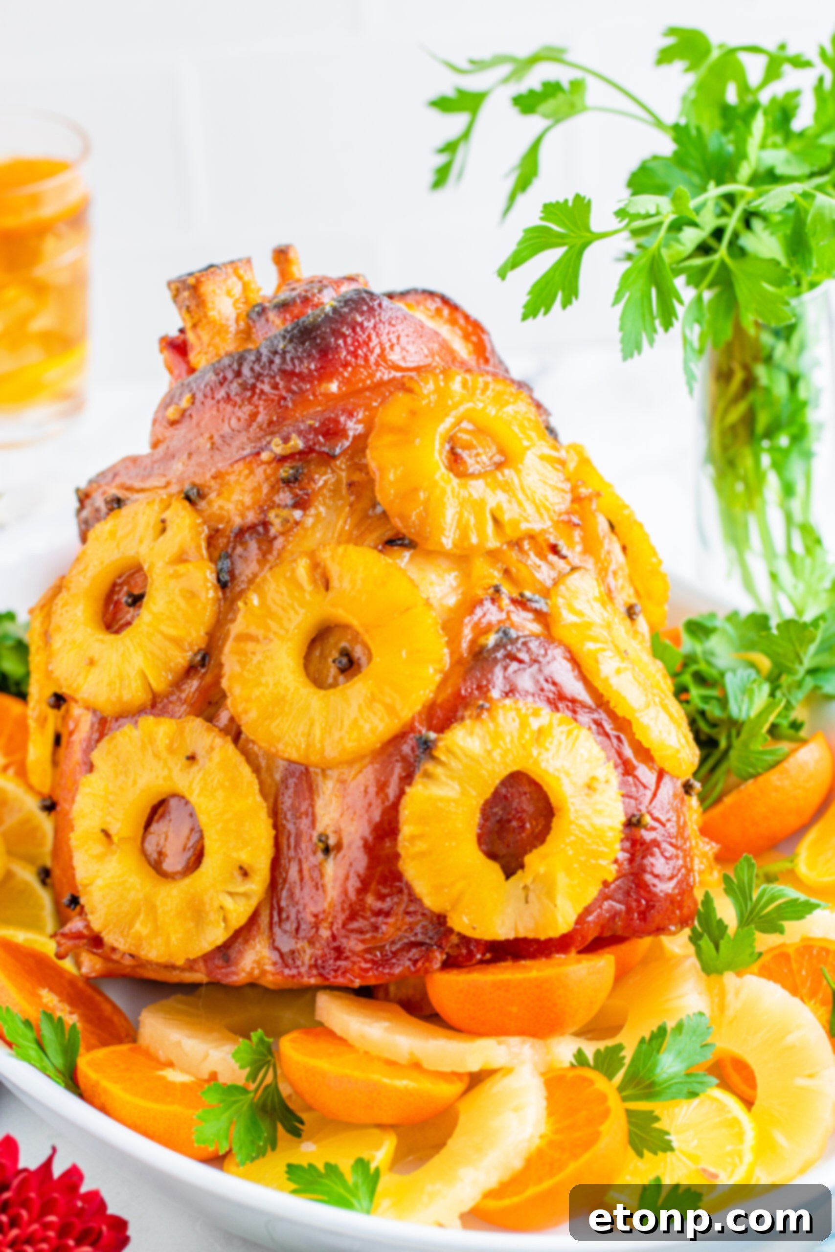 Pineapple Baked Ham covered in pineapple on a large white dish with oranges and pineapple slices lining the bottom.