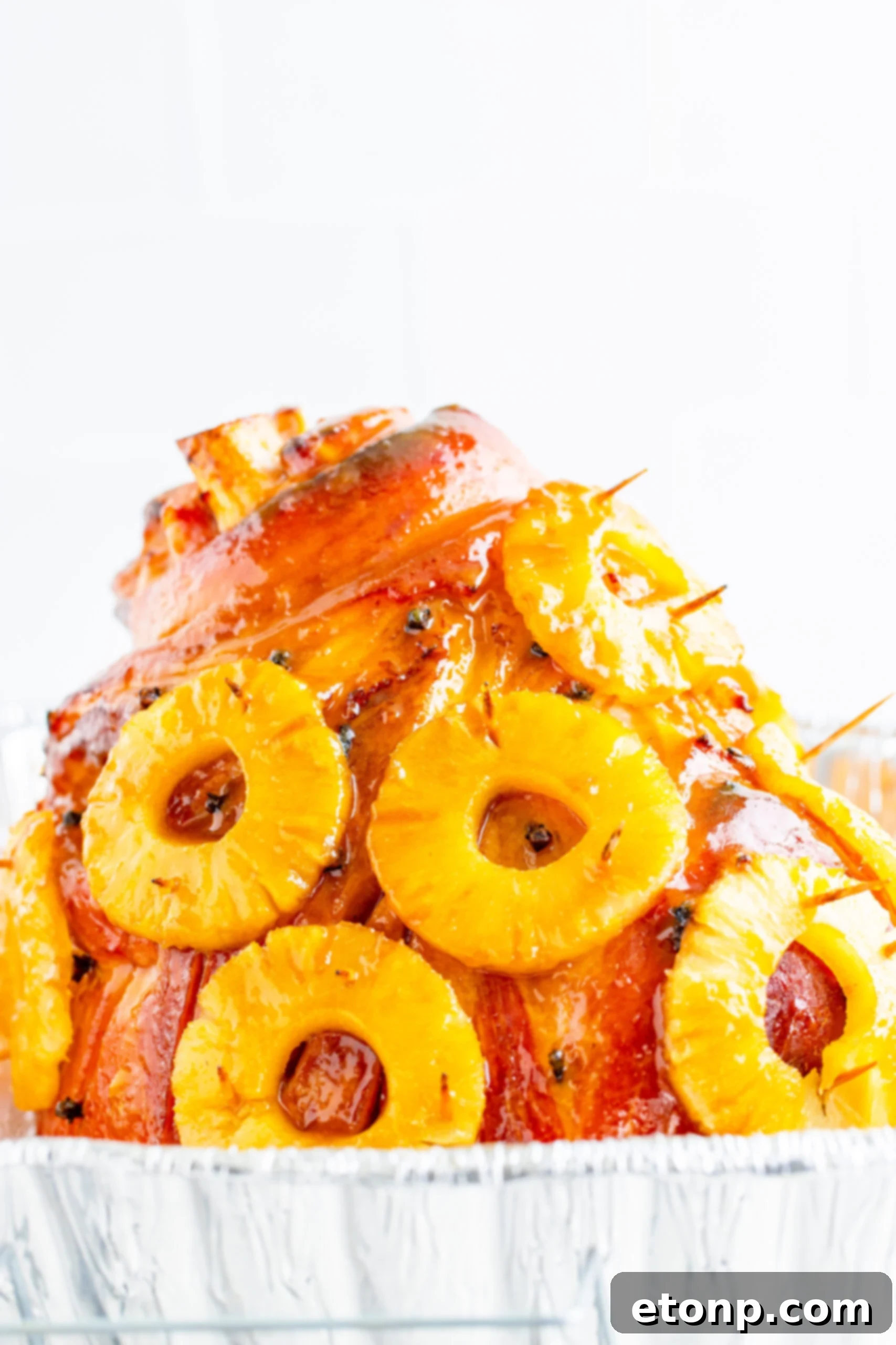Pineapple Baked Ham covered in pineapple on a large white dish with oranges and pineapple slices lining the bottom.