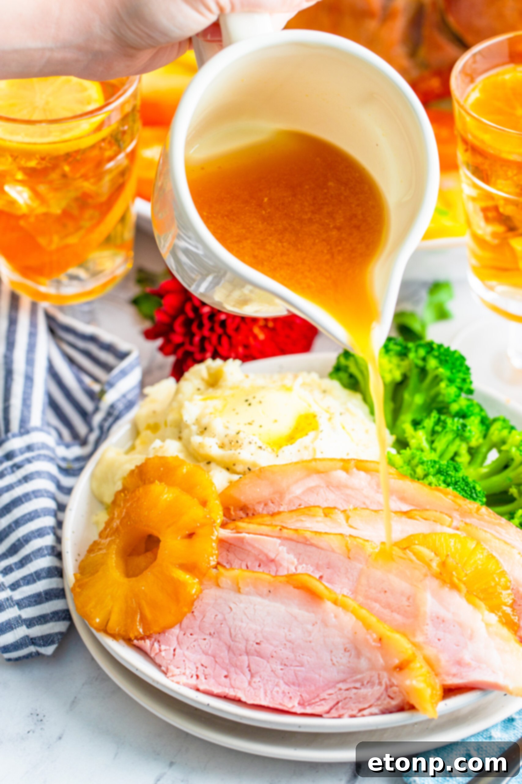 pouring gravy over top the sliced and plated pineapple baked ham. 