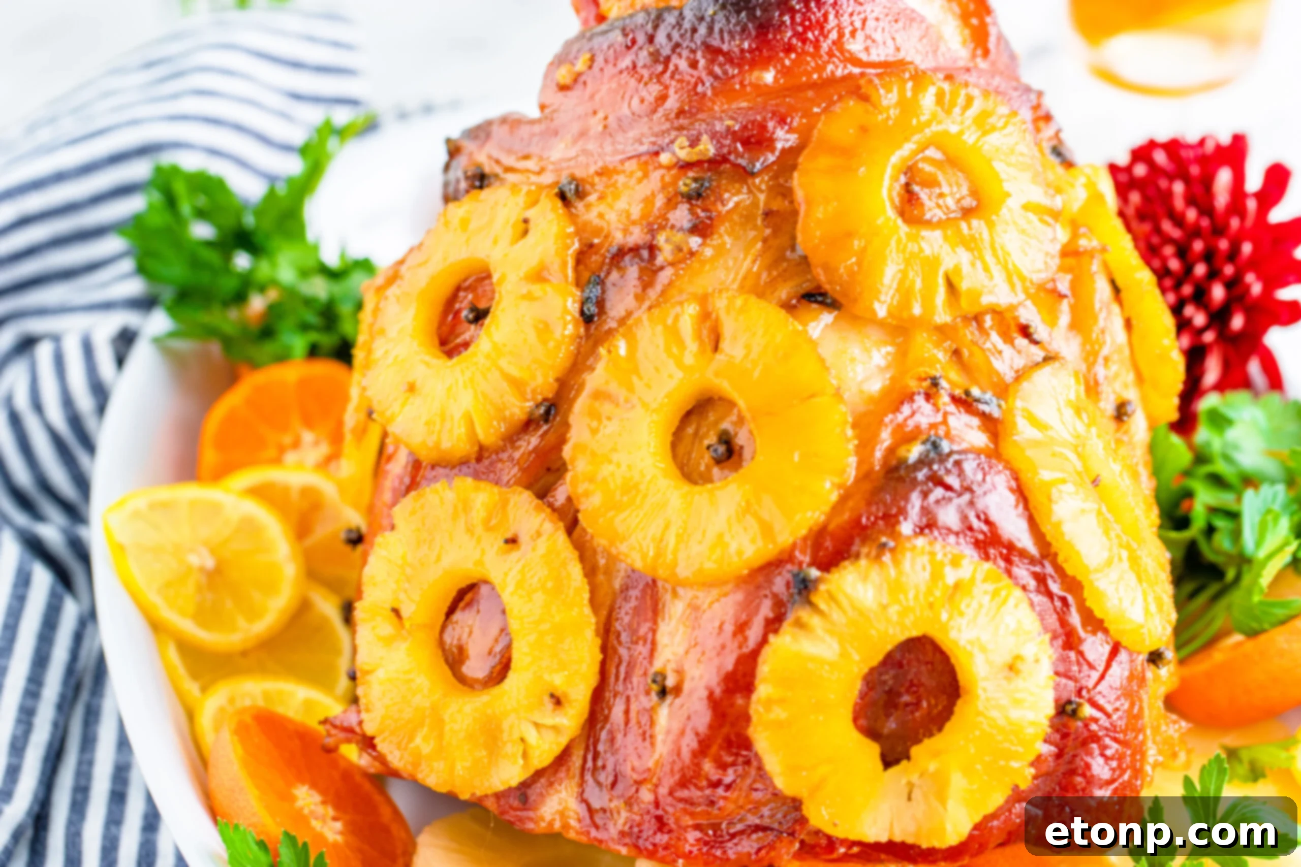 Pineapple Baked Ham covered in pineapple on a large white dish with oranges and pineapple slices lining the bottom.