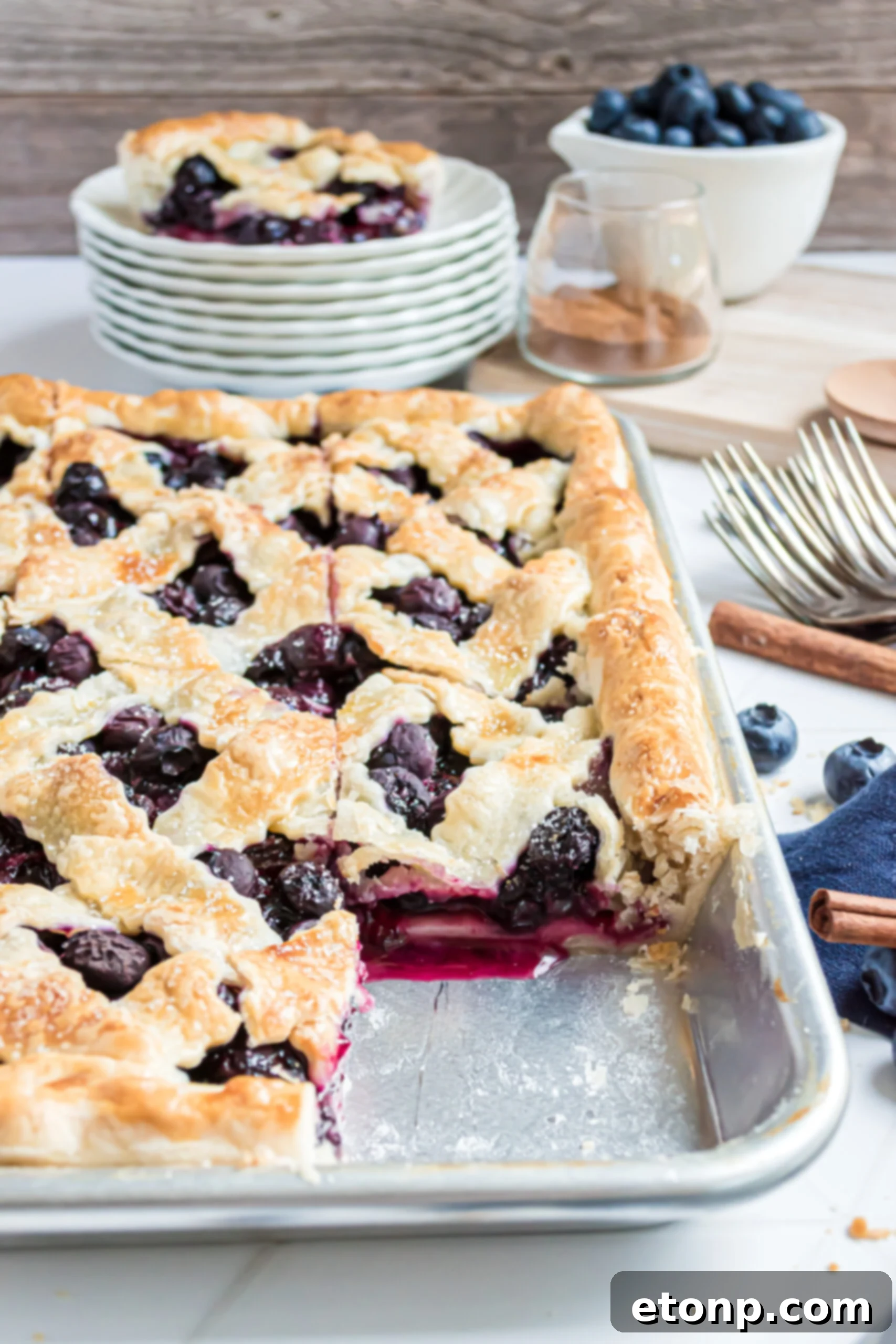 The golden-brown, rectangular Blueberry Slab Pie cooling in a silver baking pan after being freshly baked, displaying its beautiful lattice top.
