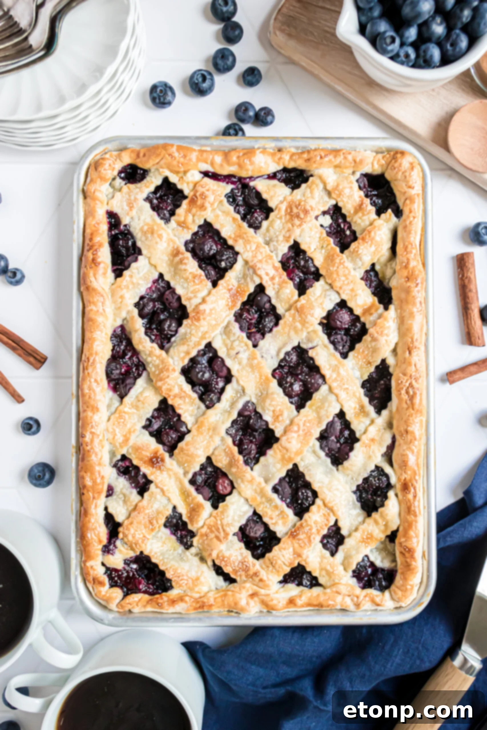 An inviting overhead shot of the complete Blueberry Slab Pie, baked to golden perfection with a beautiful lattice top, in a sleek silver baking dish, ready to be sliced.