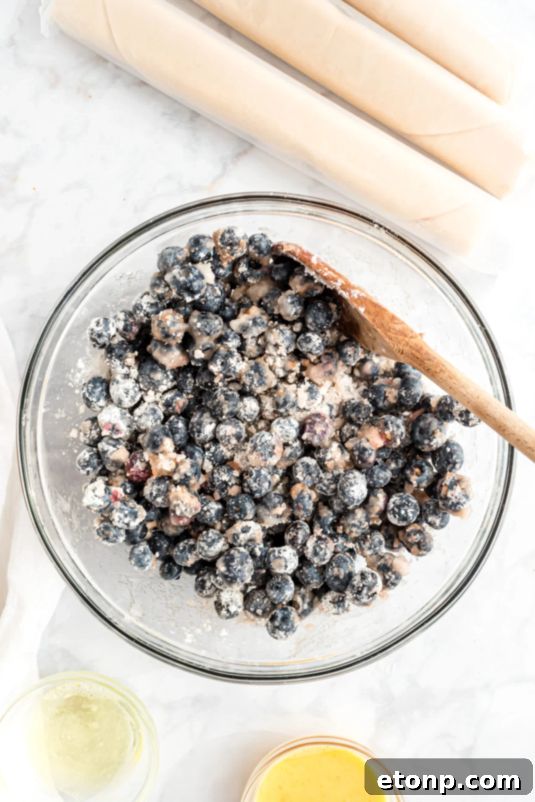 An overhead view of the vibrant blueberry pie filling ingredients, mixed in a large bowl, showcasing the fresh fruit and spices before being added to the crust.