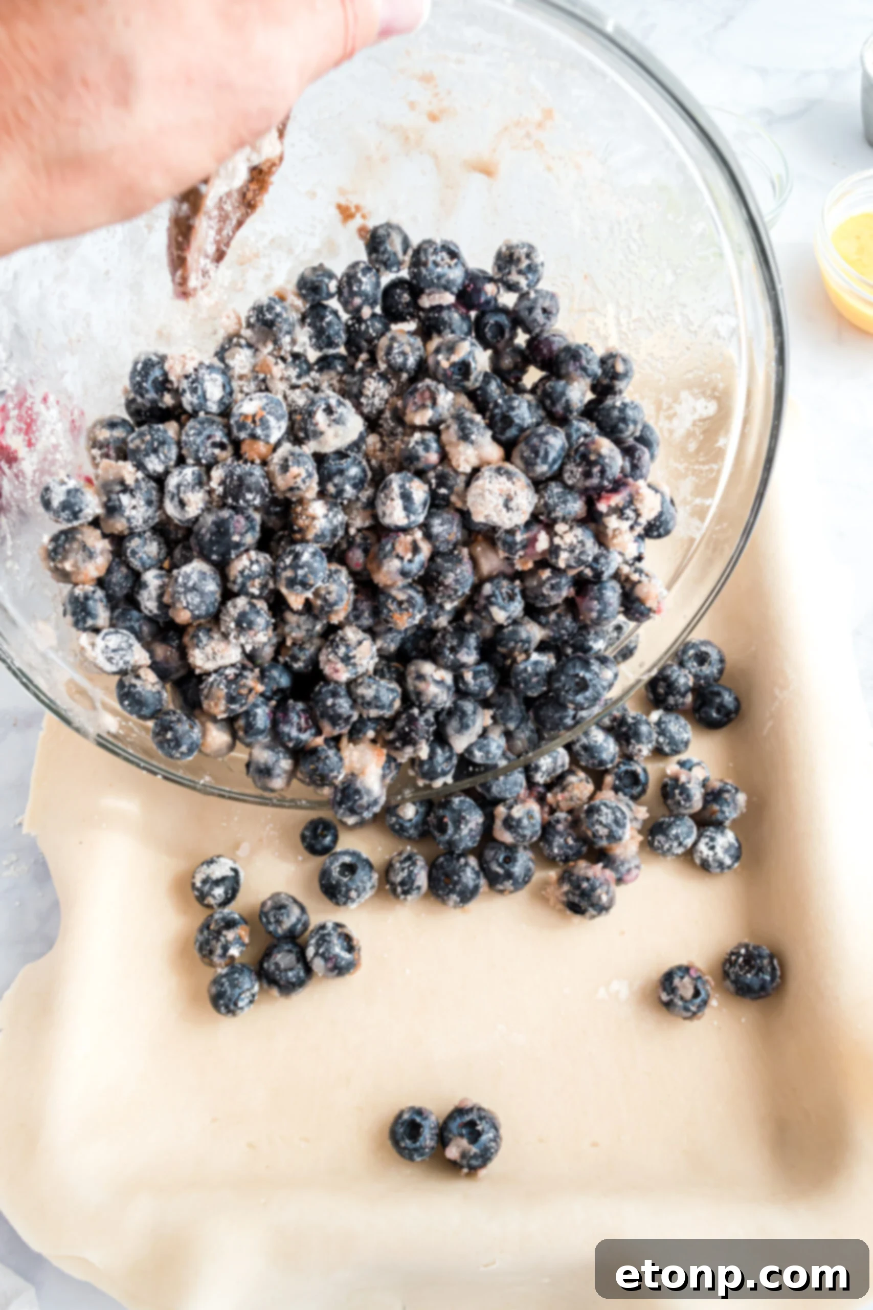 The process of pouring the shimmering, thick blueberry filling into the ready-prepared pie crust nestled in a baking pan, creating an even layer.