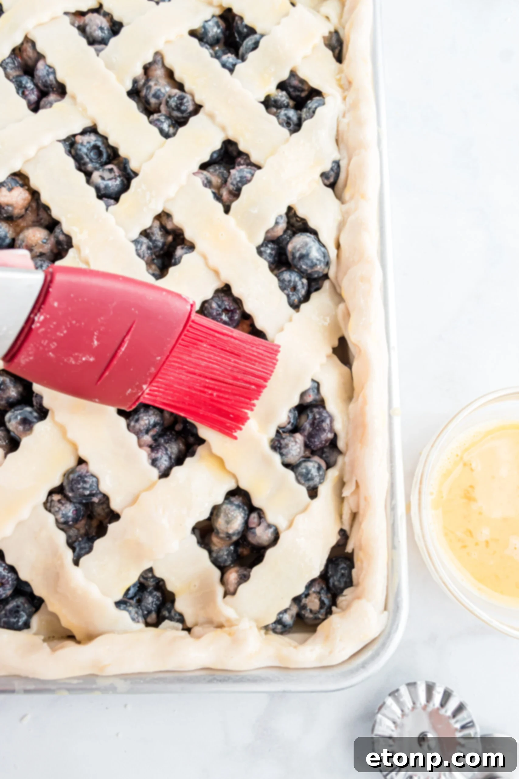 Brushing a golden egg wash onto the intricate lattice crust of the pie before baking, ensuring a beautiful, glossy finish and a perfectly browned top.