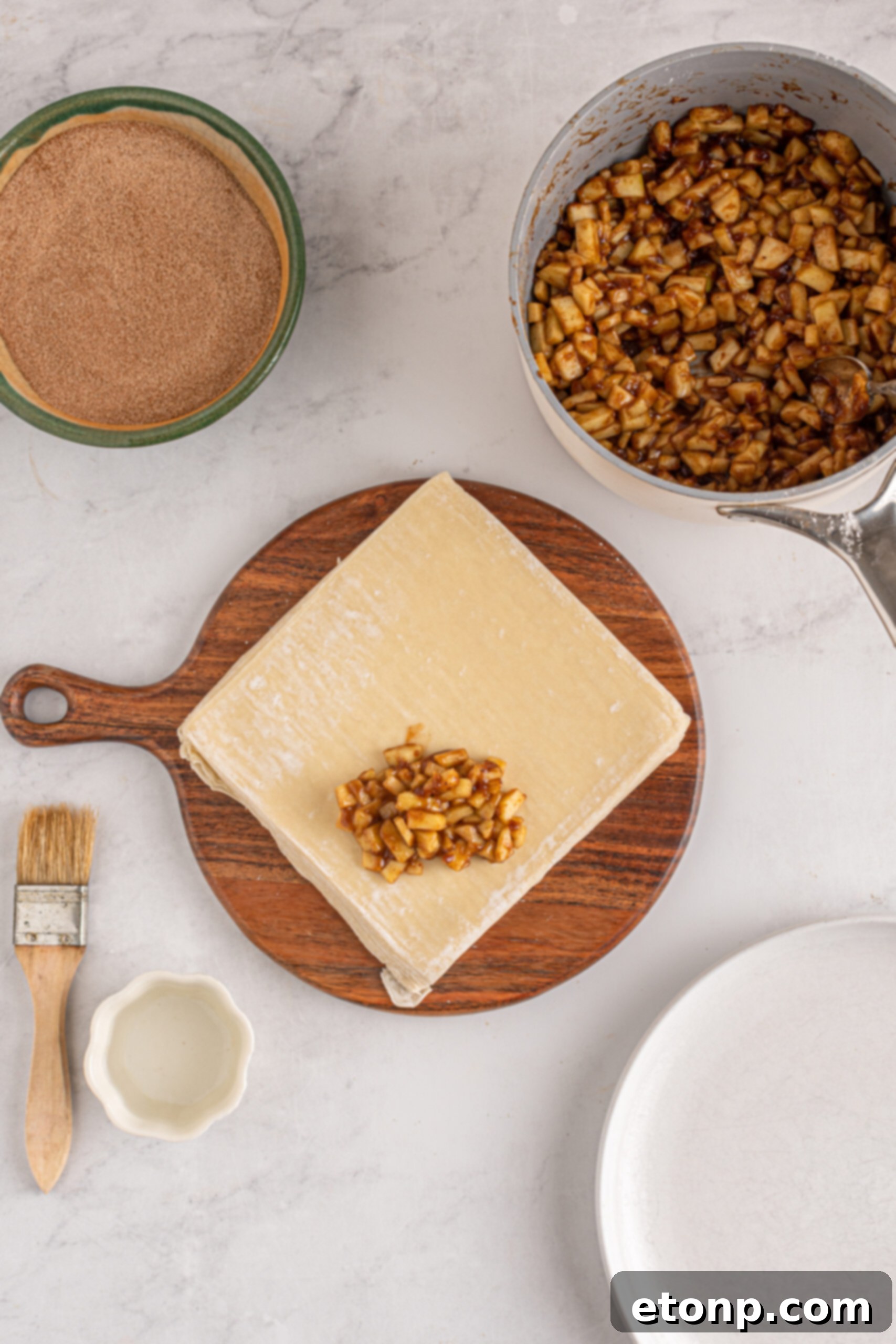 An overhead shot showcasing the careful process of wrapping apple pie egg rolls on a clean kitchen surface, illustrating how the filling is encased in the wrapper.
