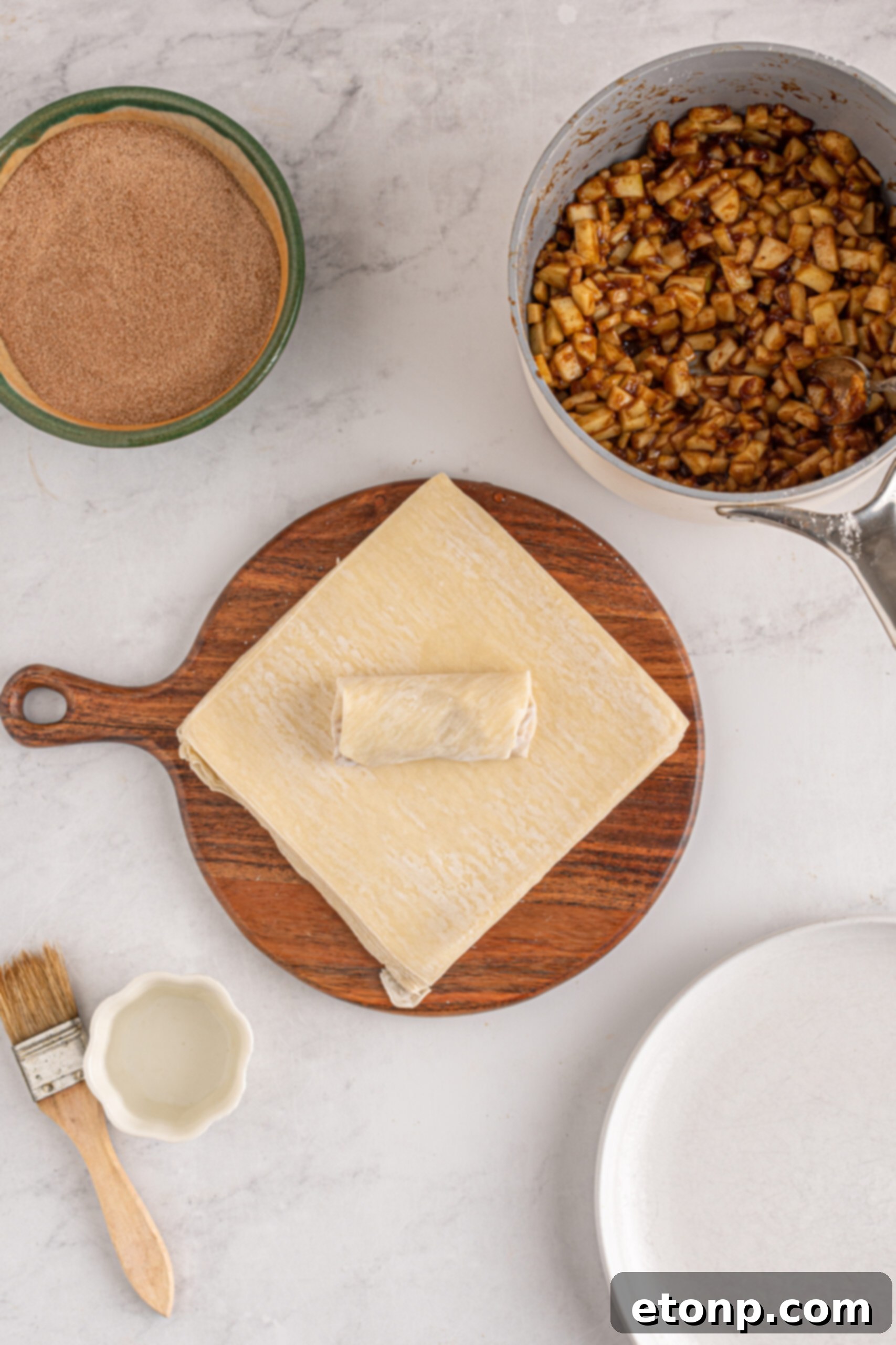 A close-up, overhead view of a perfectly wrapped apple pie egg roll, neatly folded and ready for frying, showcasing the craftsmanship involved.