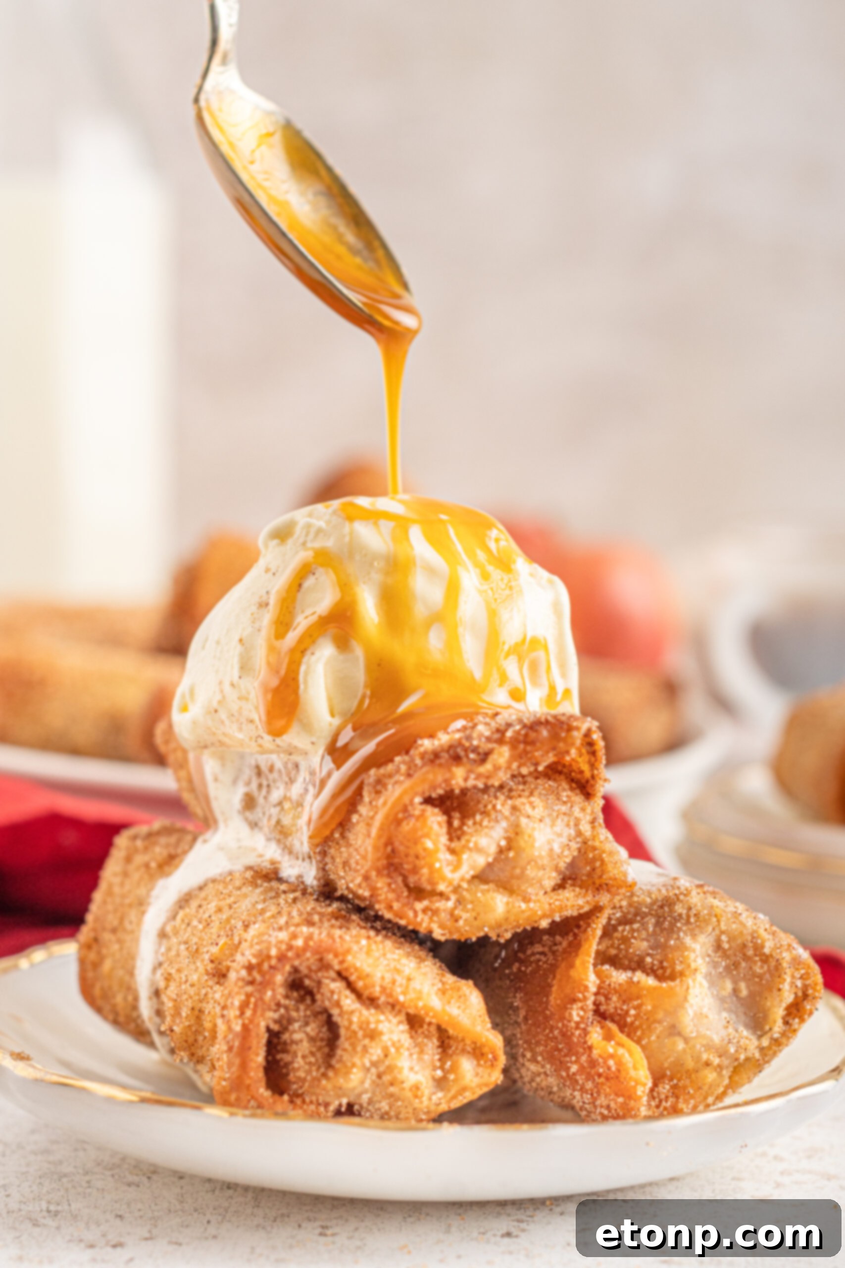 Three perfectly fried Egg Rolls artfully stacked on a crisp white plate, generously adorned with a dollop of creamy vanilla ice cream and a luxurious cascade of caramel sauce, highlighting a delectable dessert creation.
