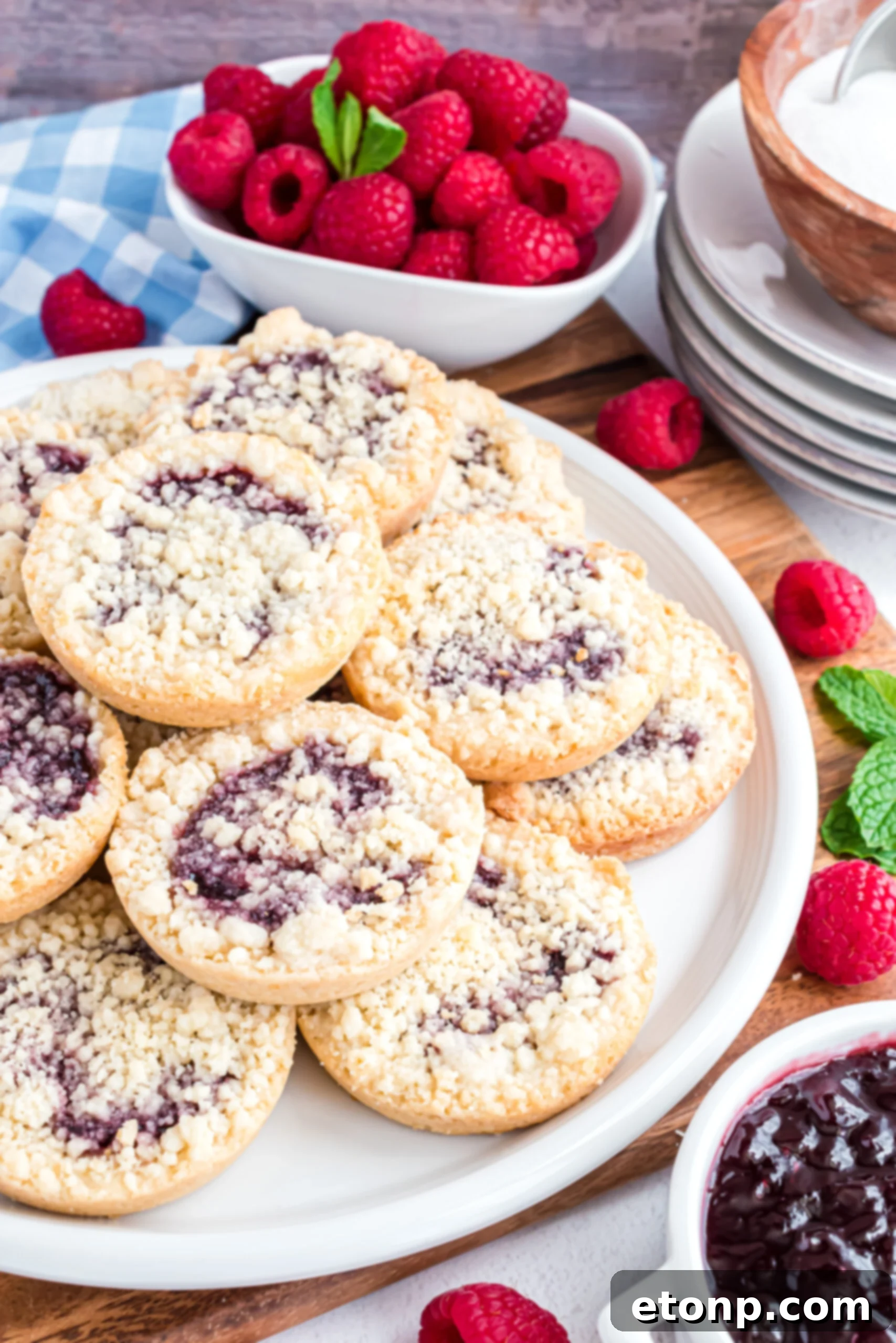 Raspberry Cookies stacked on a white plate on a wooden cutting board with fresh raspberries in the background.