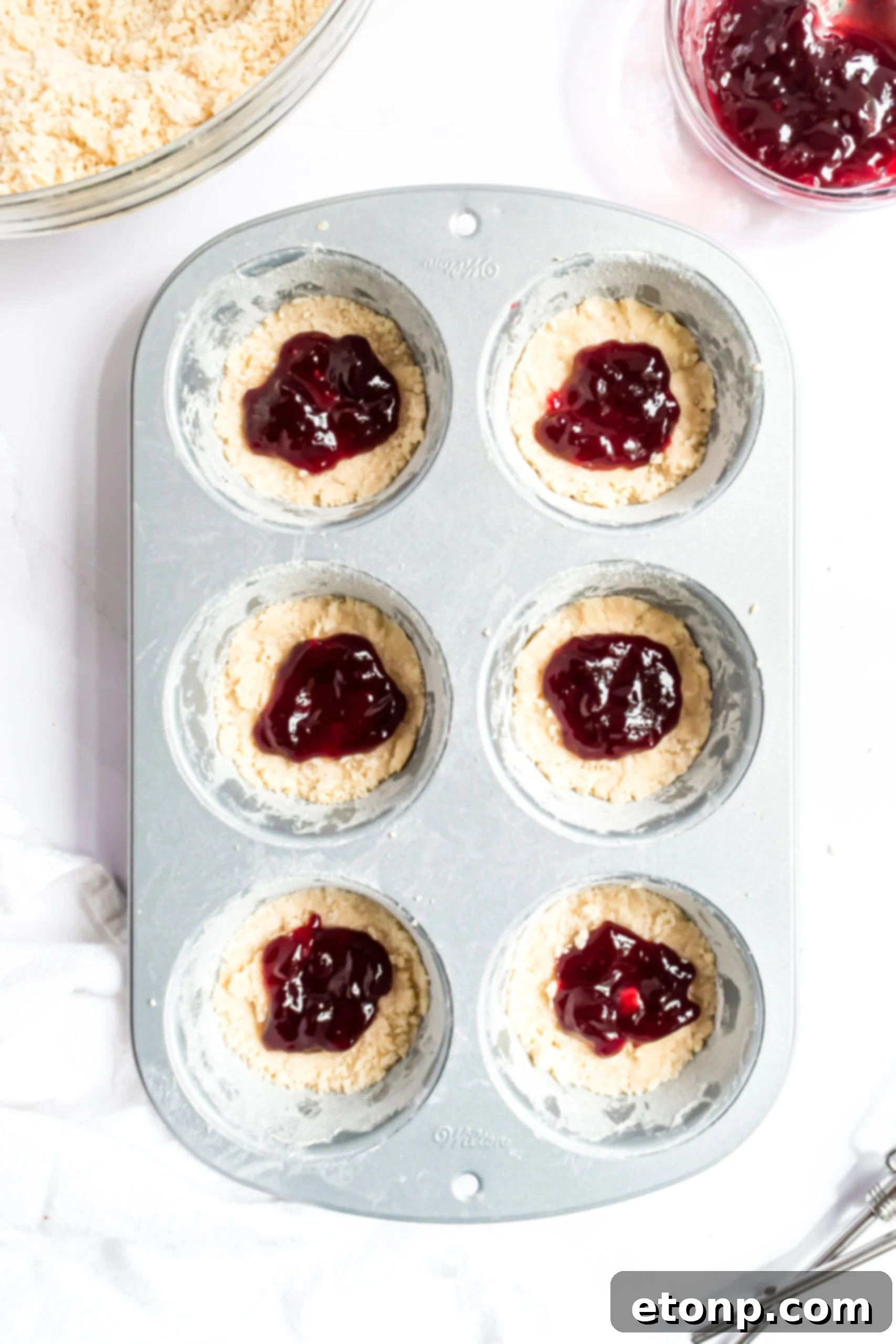 Overhead shot of the raspberry filling being added to the muffin tins.