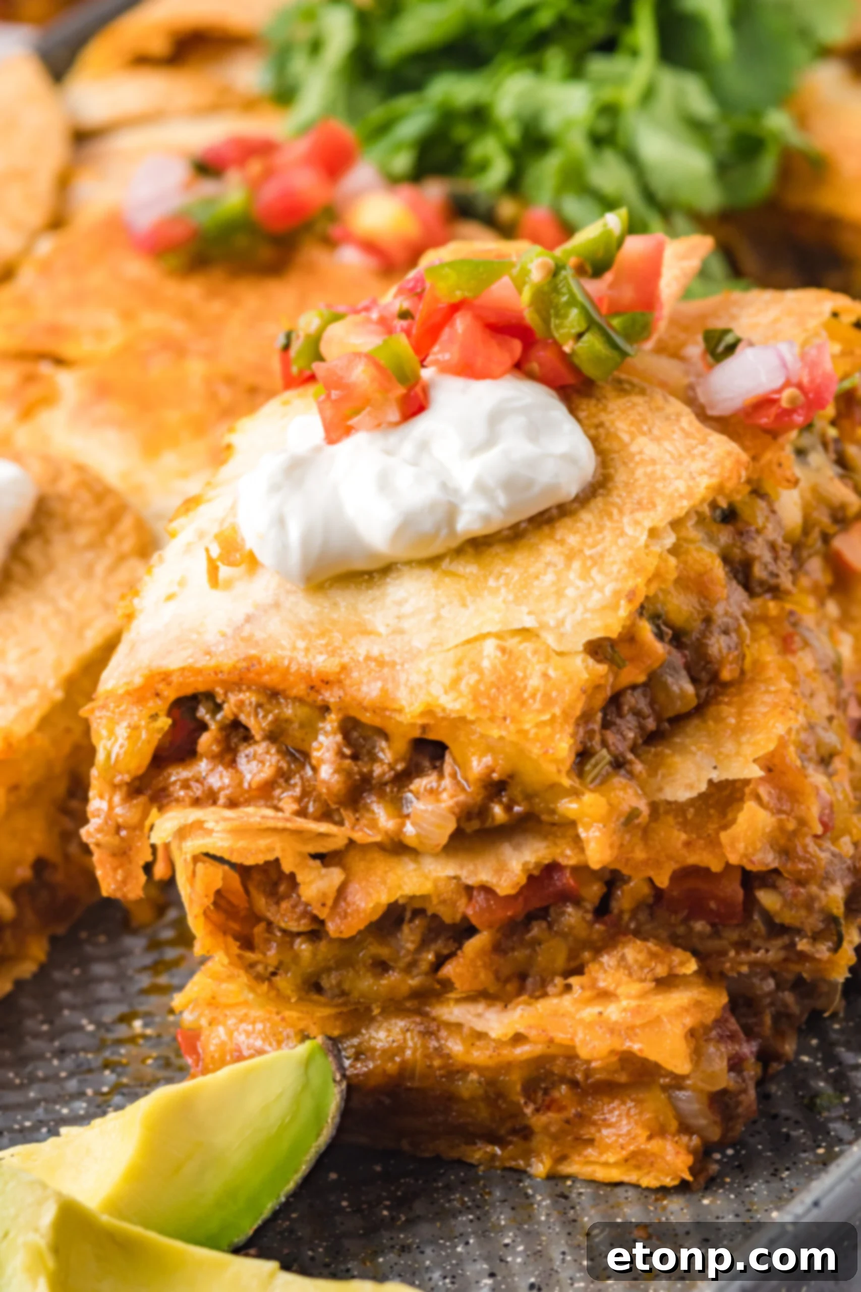 Close up of three slices of sheet pan tacos stacked on the baking sheet topped with sour cream and Pico de Gallo 