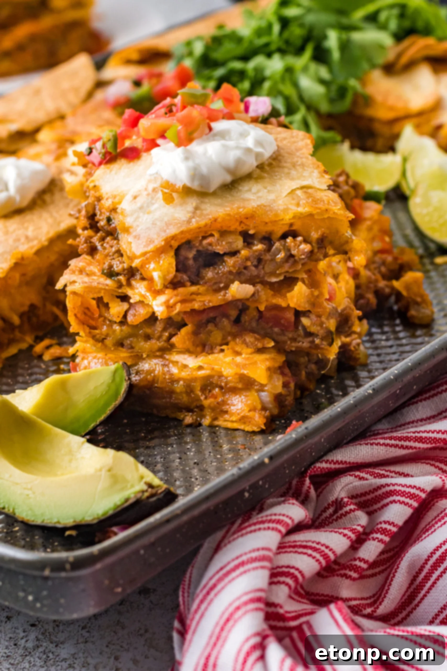 Three slices of sheet pan tacos stacked on the baking sheet topped with sour cream and Pico de Gallo