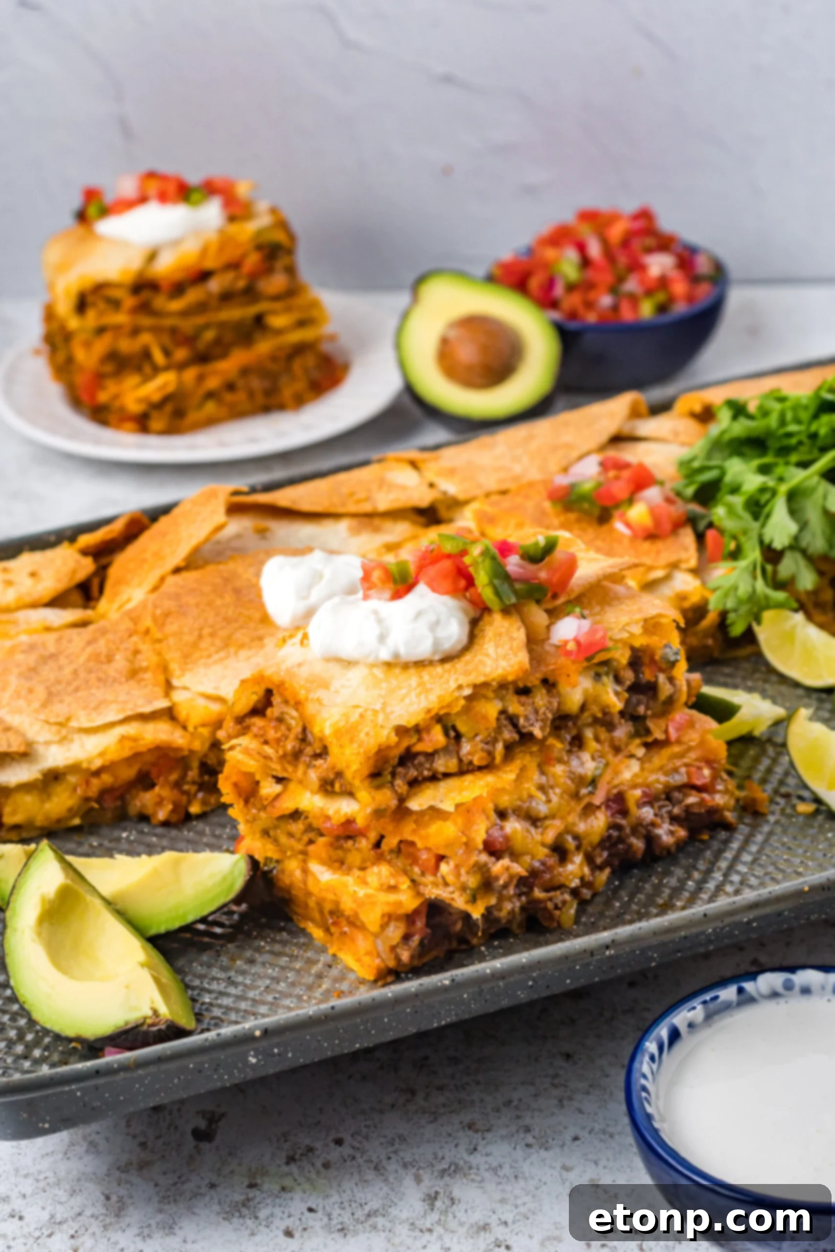 Three slices of sheet pan tacos stacked on the baking sheet topped with sour cream and Pico de Gallo