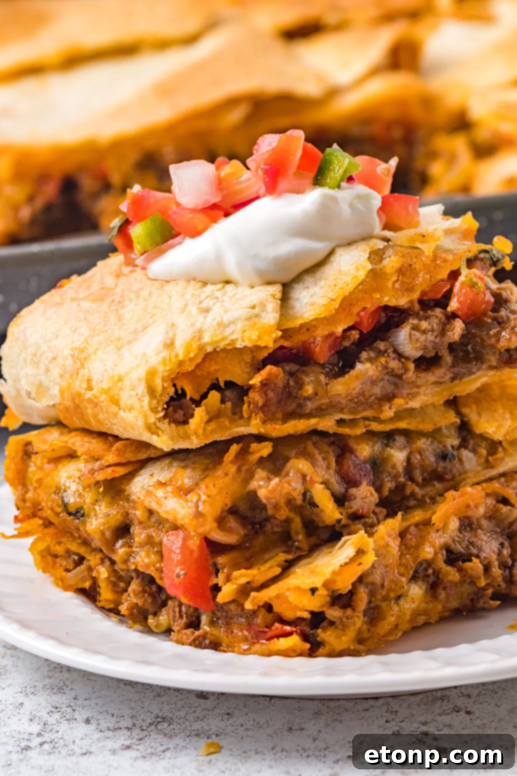 Three slices of sheet pan tacos stacked on a white plate and topped with Pico de Gallo. 