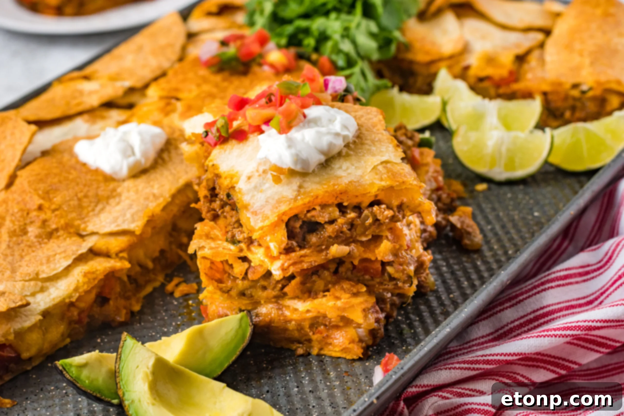 Three slices of sheet pan tacos stacked on the baking sheet topped with sour cream and Pico de Gallo