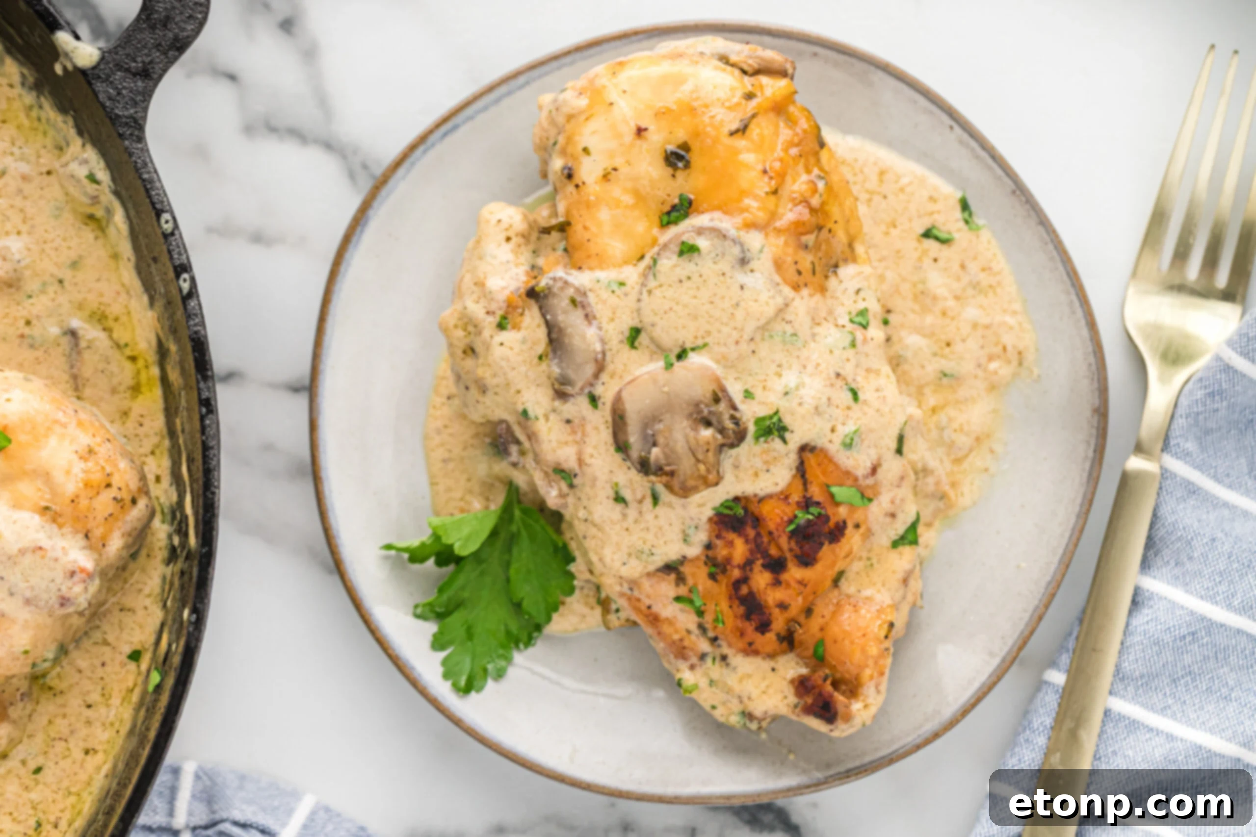 A piece of chicken on a white plate with a gold fork covered in sauce and mushrooms. 