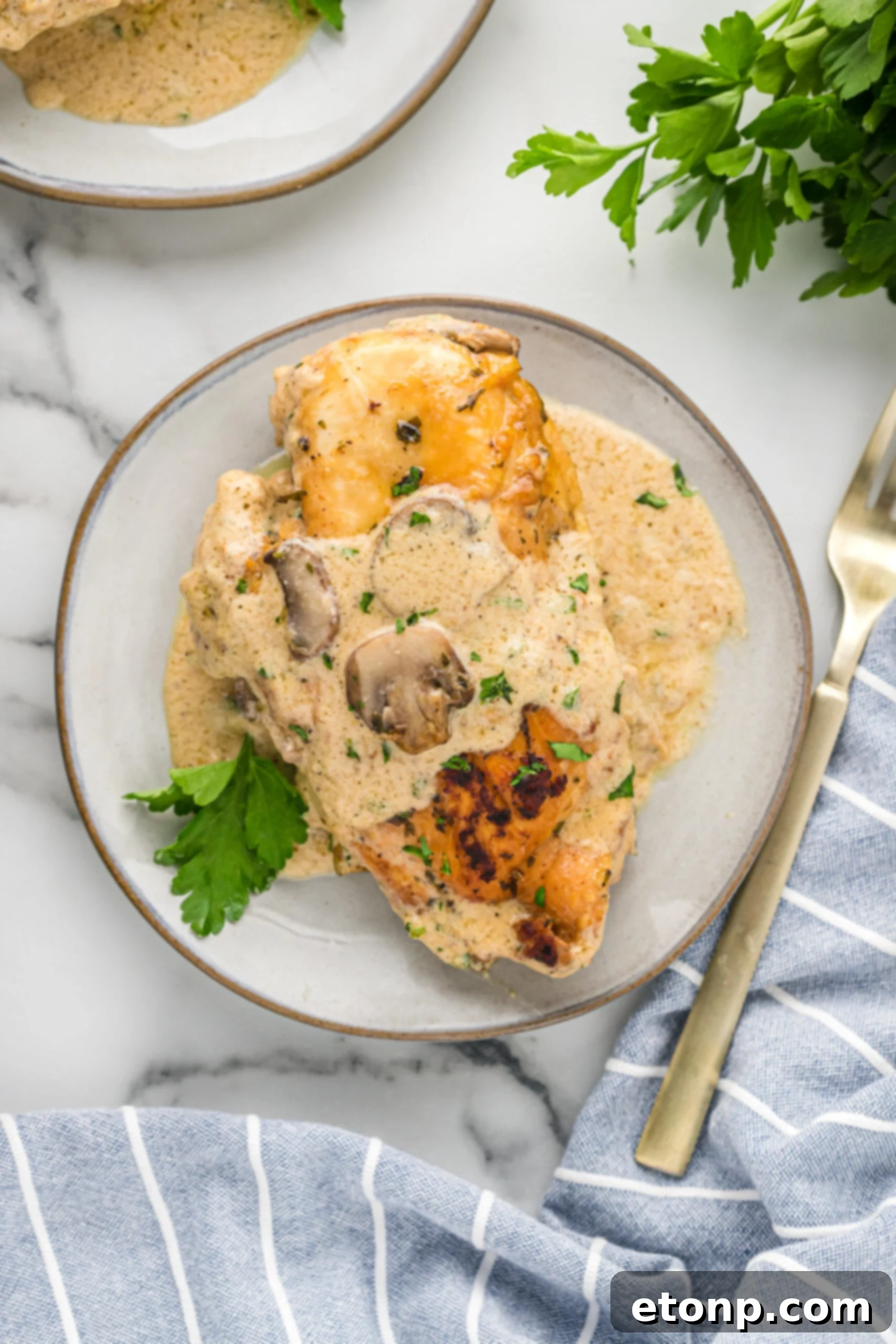 A piece of chicken on a white plate with a gold fork covered in sauce and mushrooms. 