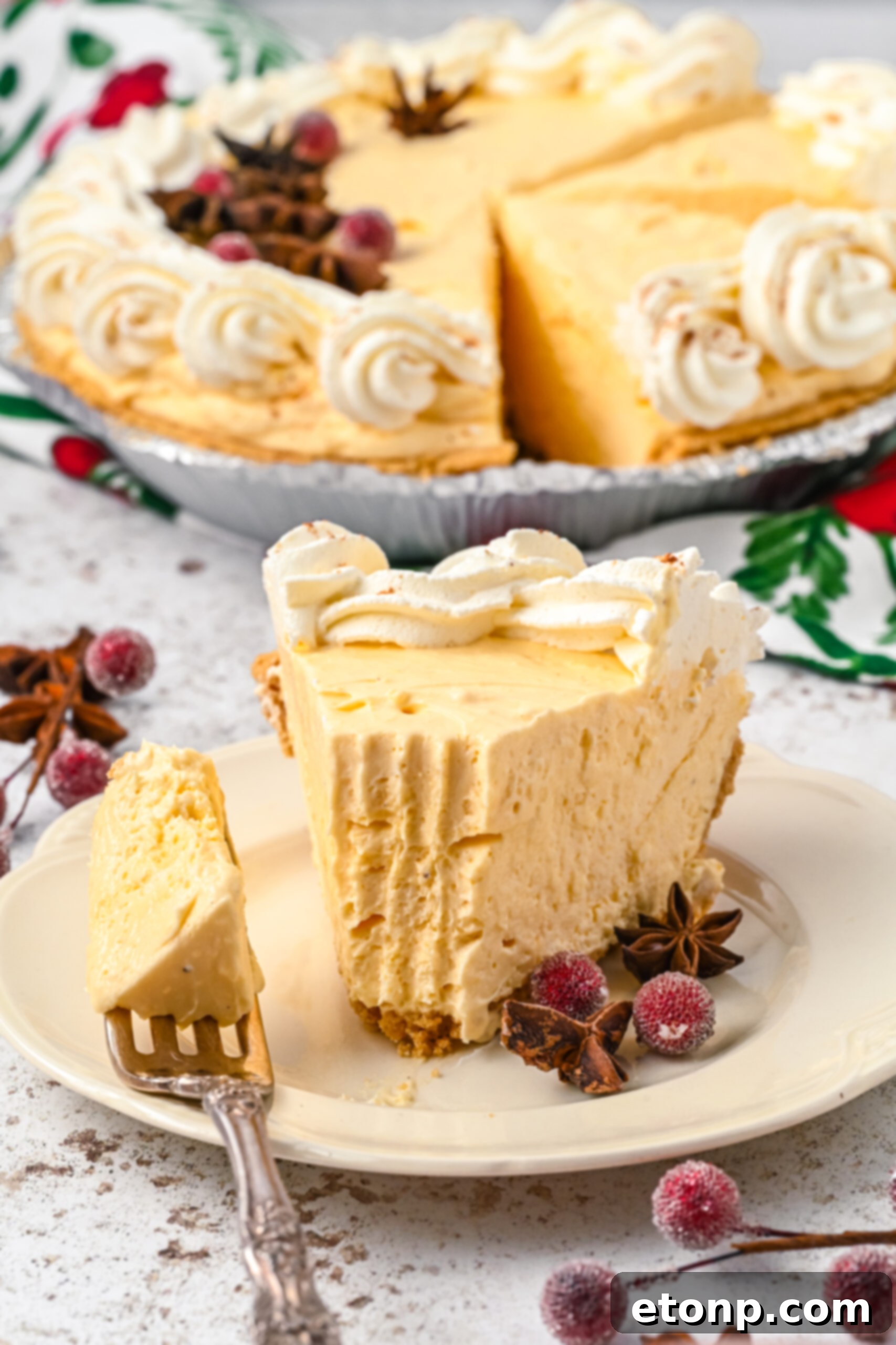 Velvety Eggnog Pie 12 A mouthwatering piece of Eggnog Pie on a white dish, with a silver fork gently removing a portion, revealing the fluffy, creamy interior of the pie.