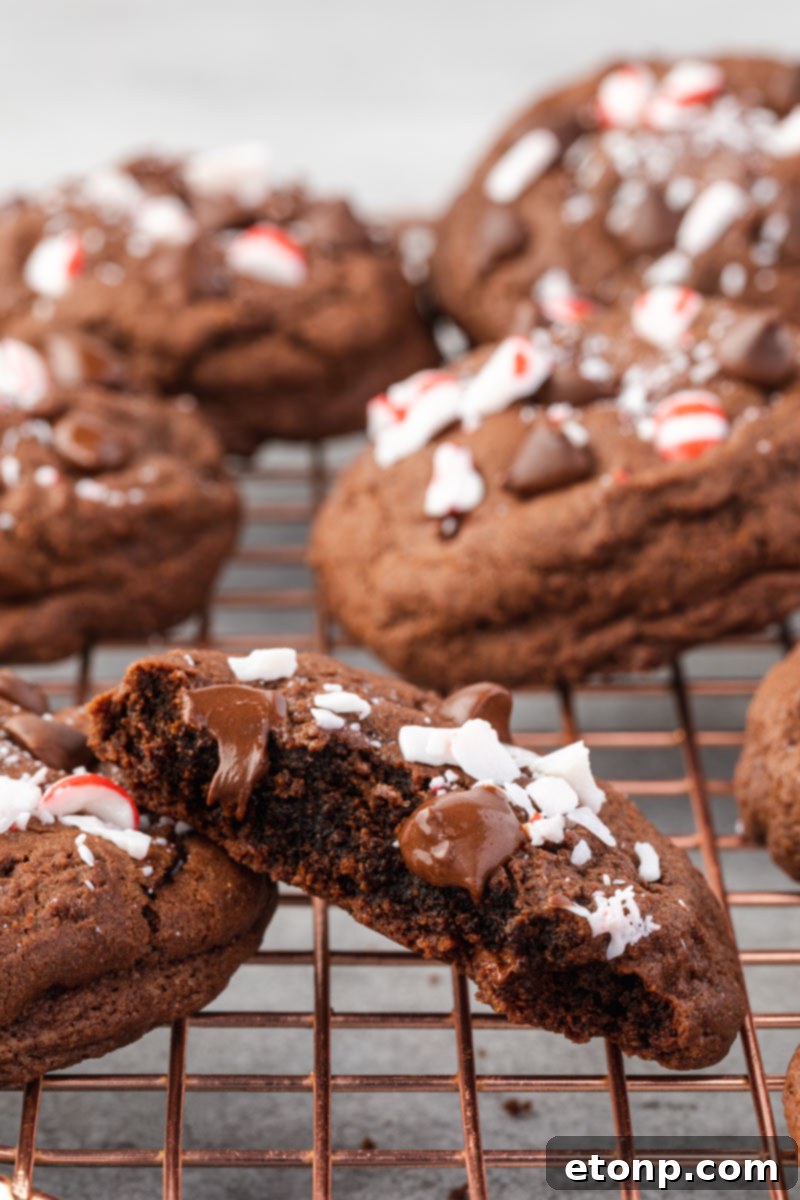 A Chocolate Peppermint Cookie carefully cut in half on a rose gold cooling rack, highlighting its soft, chewy center and perfect texture.