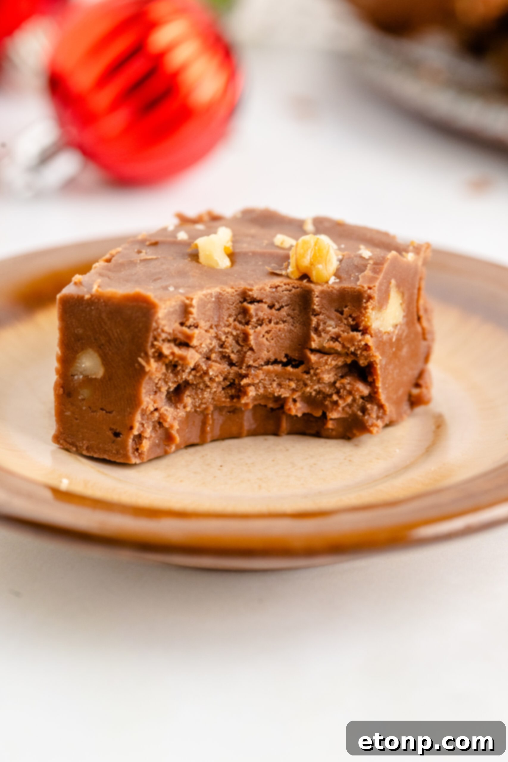 A piece of fantasy fudge on a brown plate with a bite removed showing the inside. 