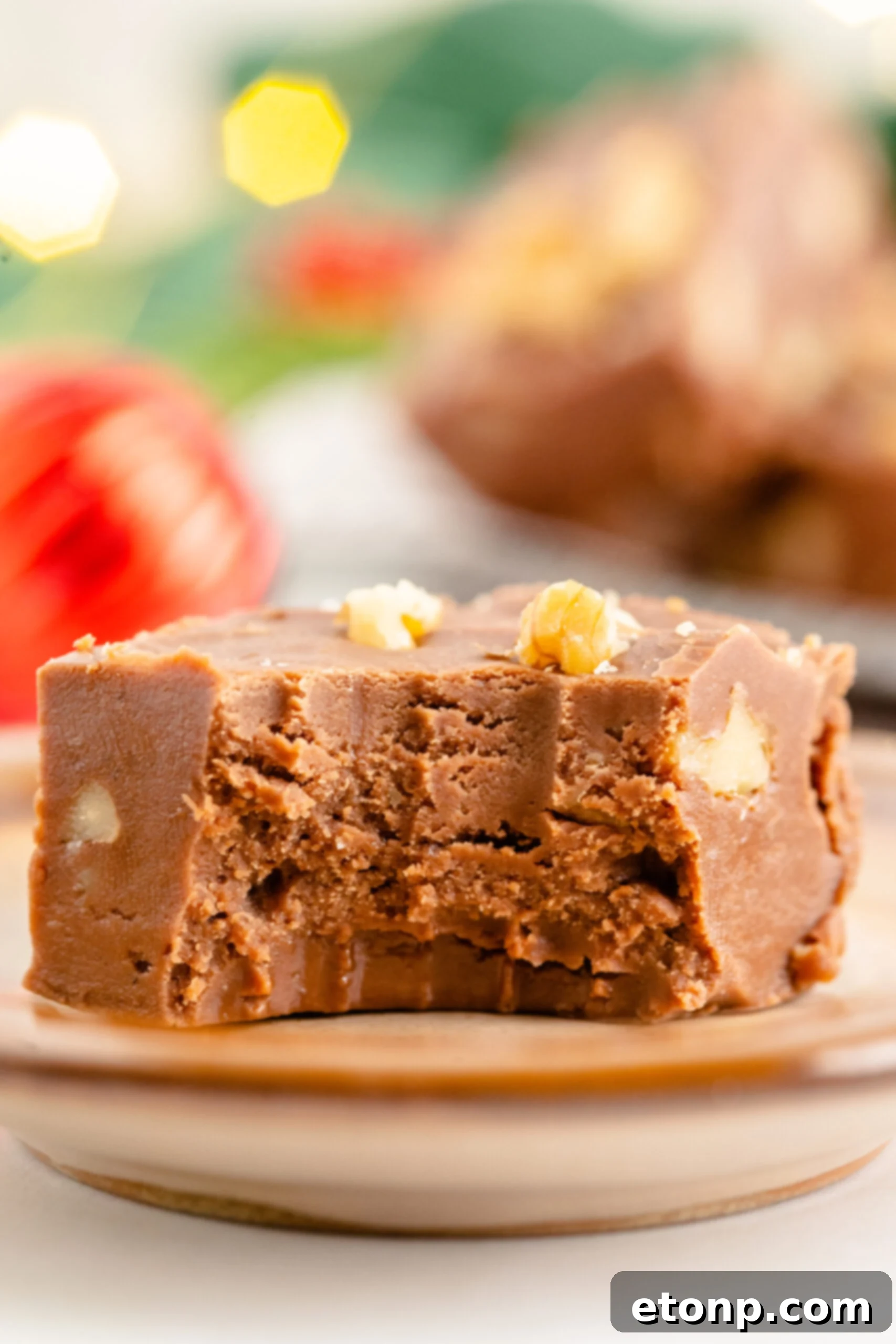 A piece of fantasy fudge on a brown plate with a bite removed showing the inside. 