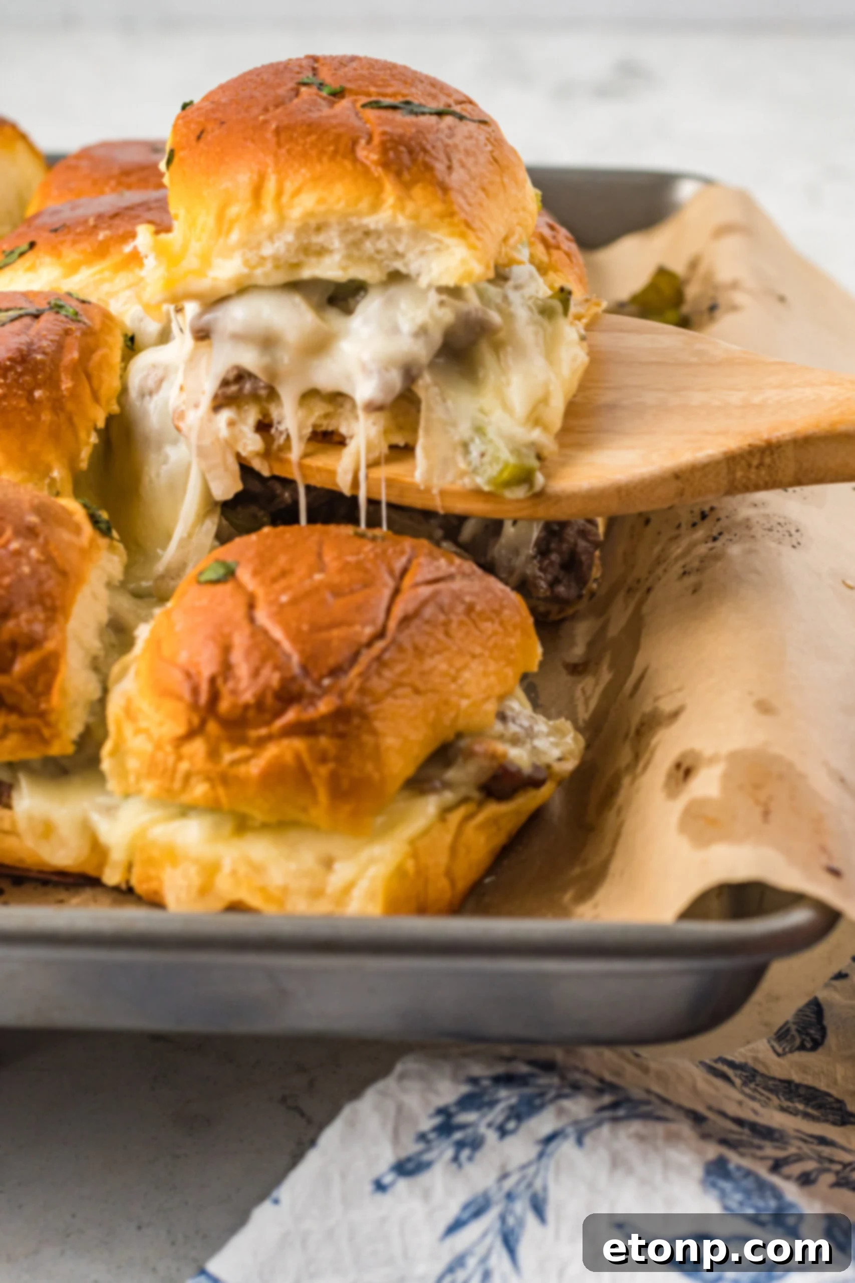 A Philly Cheesesteak Slider being removed from a baking sheet with a wooden spatula. 