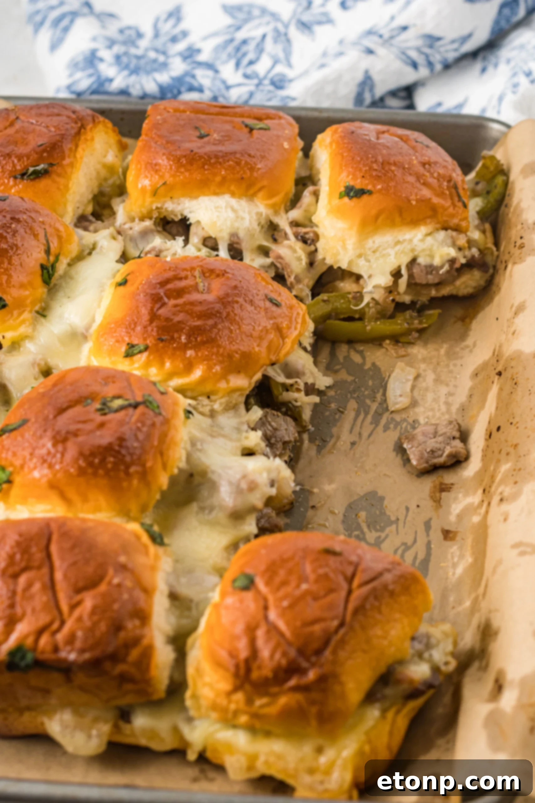 Philly Cheesesteak Sliders on a baking sheet with two removed. 