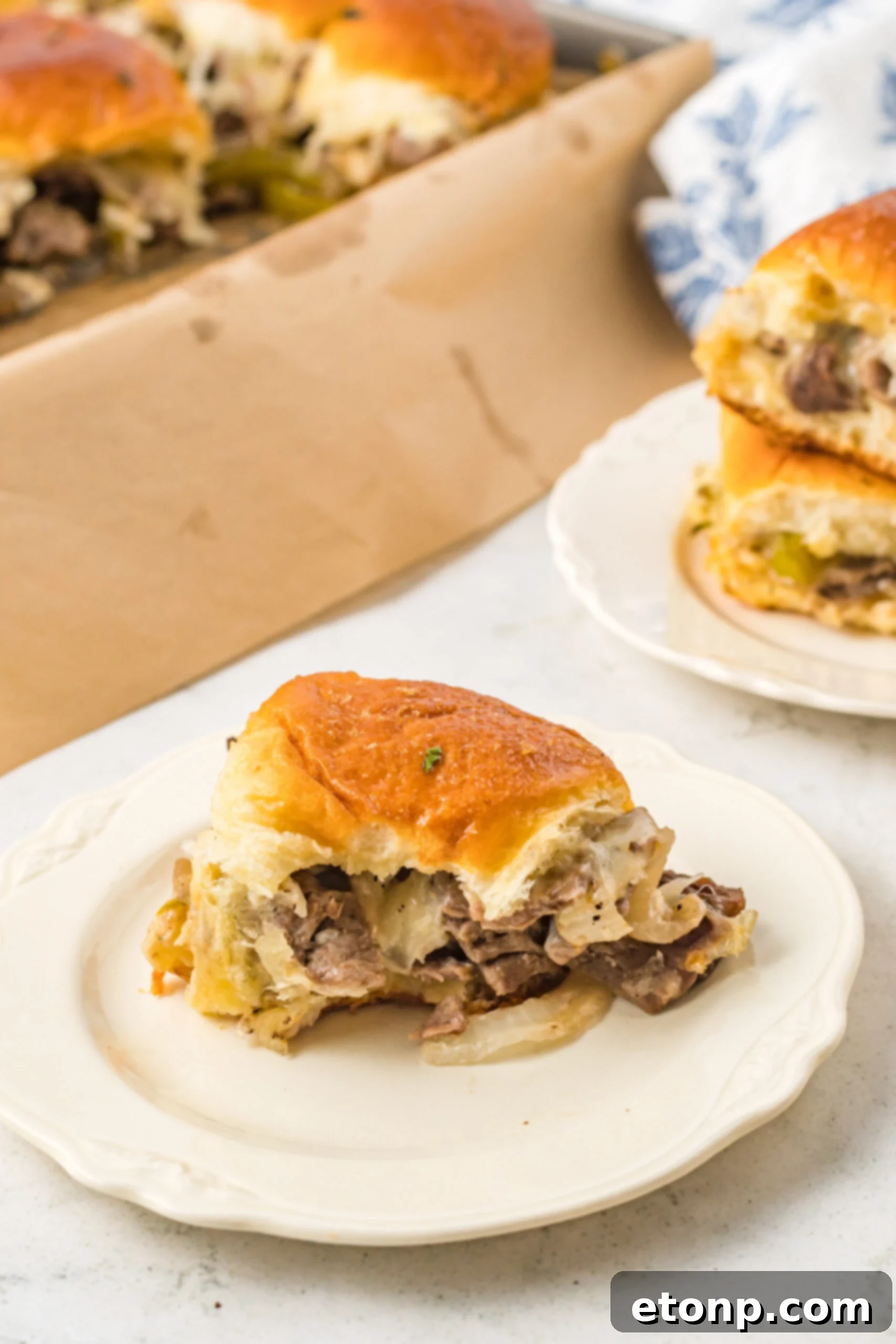 One slider on a white plate with a bite removed showing the cheesy inside. 