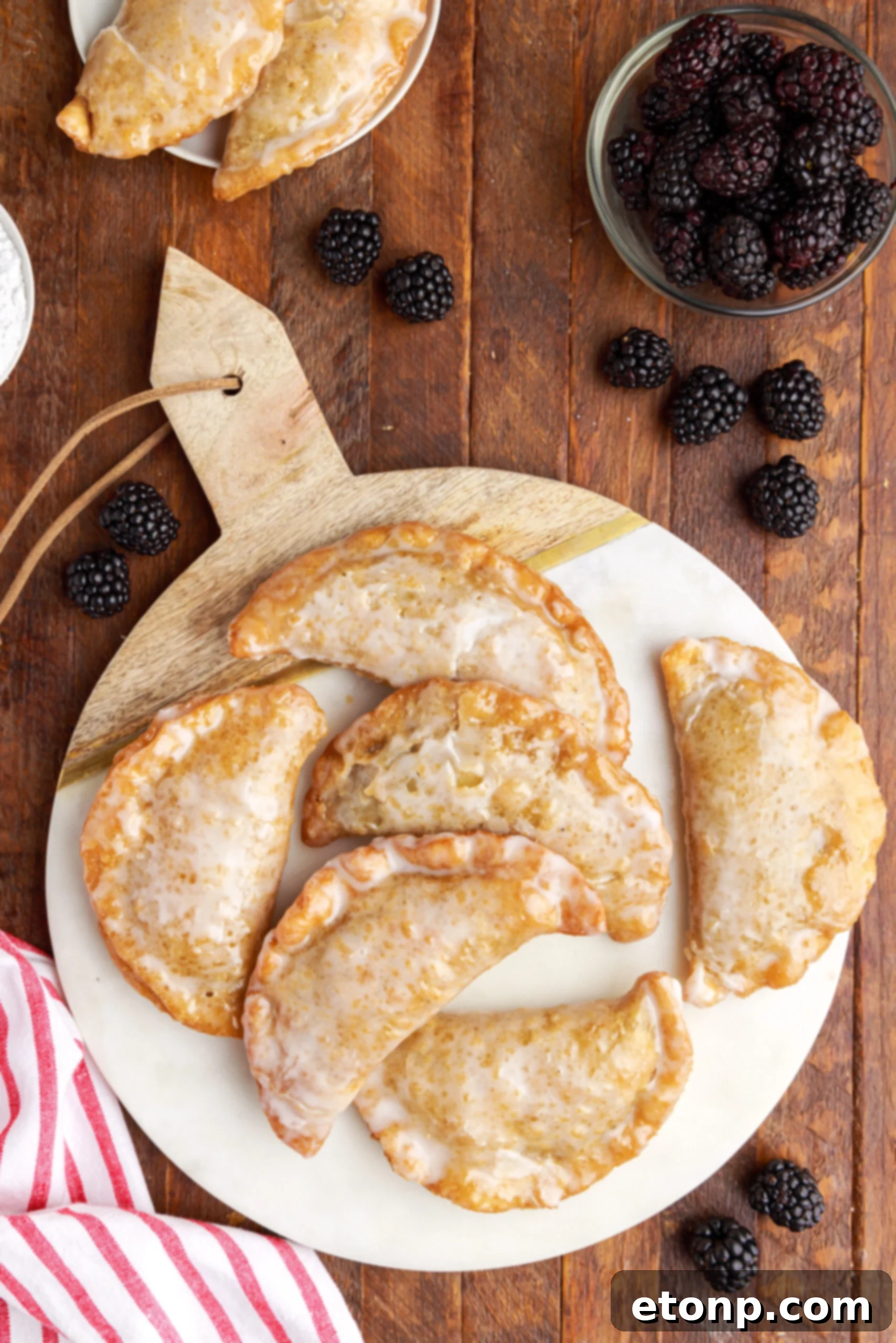 Rustic Blackberry Turnovers 5 Overhead shot of blackberry hand pies stacked on a marble serving tray with fresh blackberries on a dark wood background.