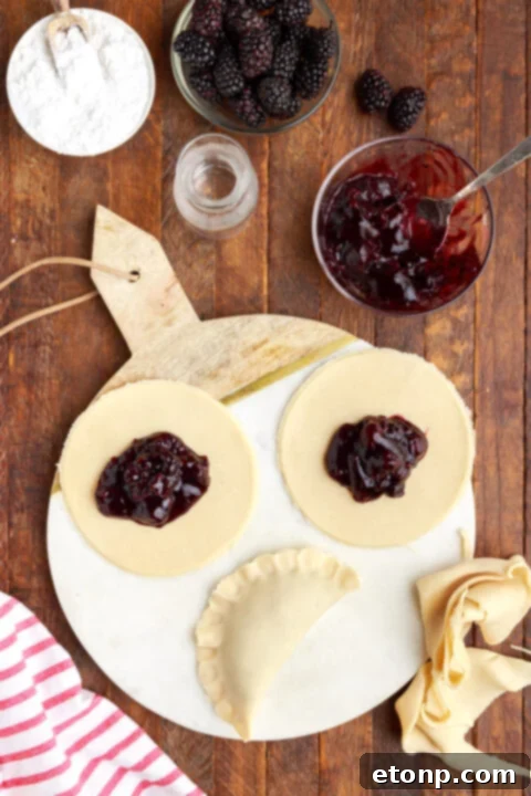 Rustic Blackberry Turnovers 9 three circle of pie dough on a marble serving tray with blackberry jam in the center of each circle. One is folded in half showing the correct way to fold a hand pie.