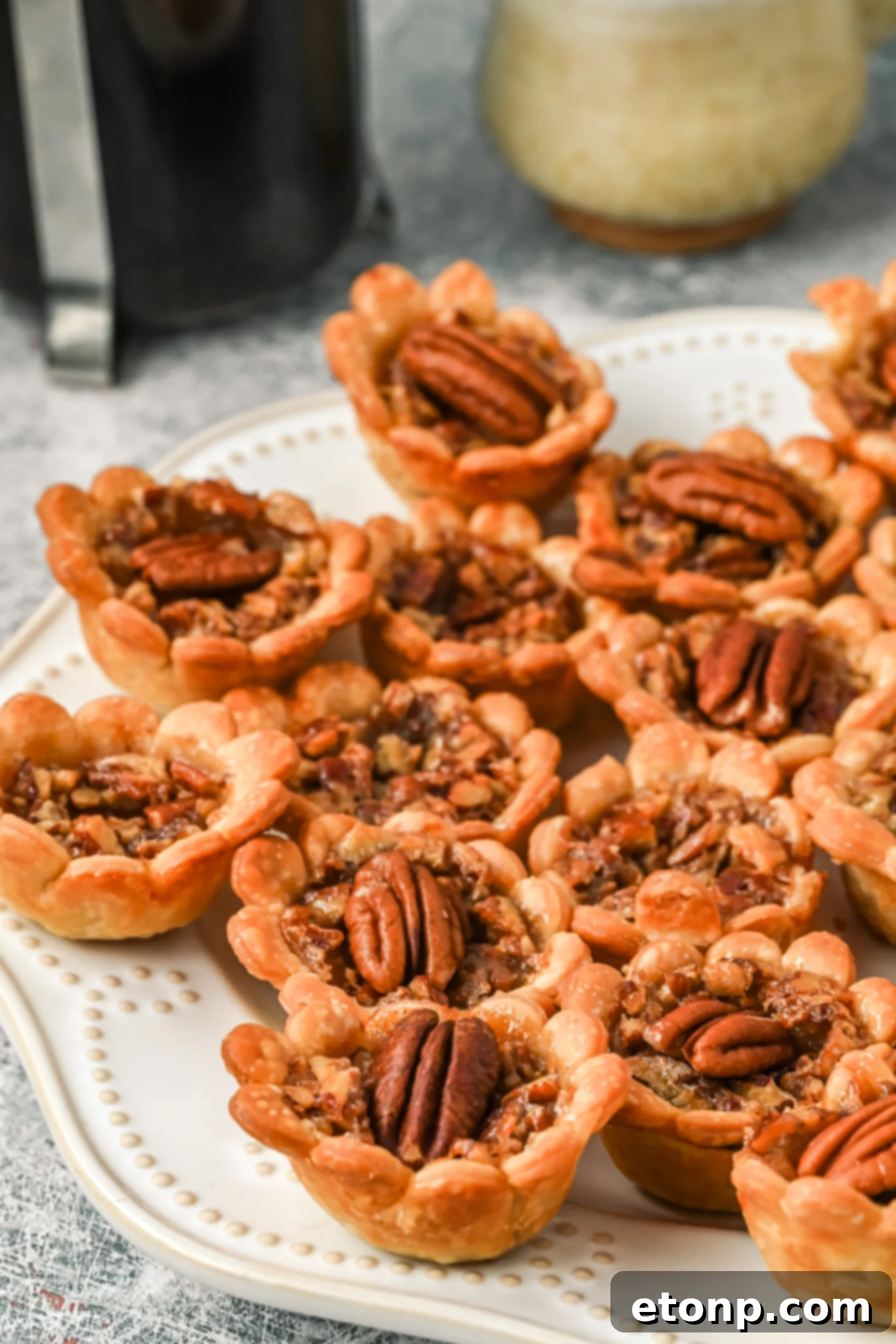 Side view of golden-brown mini pecan pies beautifully arranged on a white serving tray.
