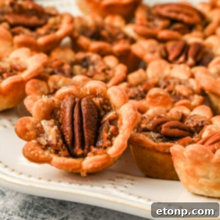 Side view of perfectly baked mini pecan pies beautifully arranged on a white serving tray.