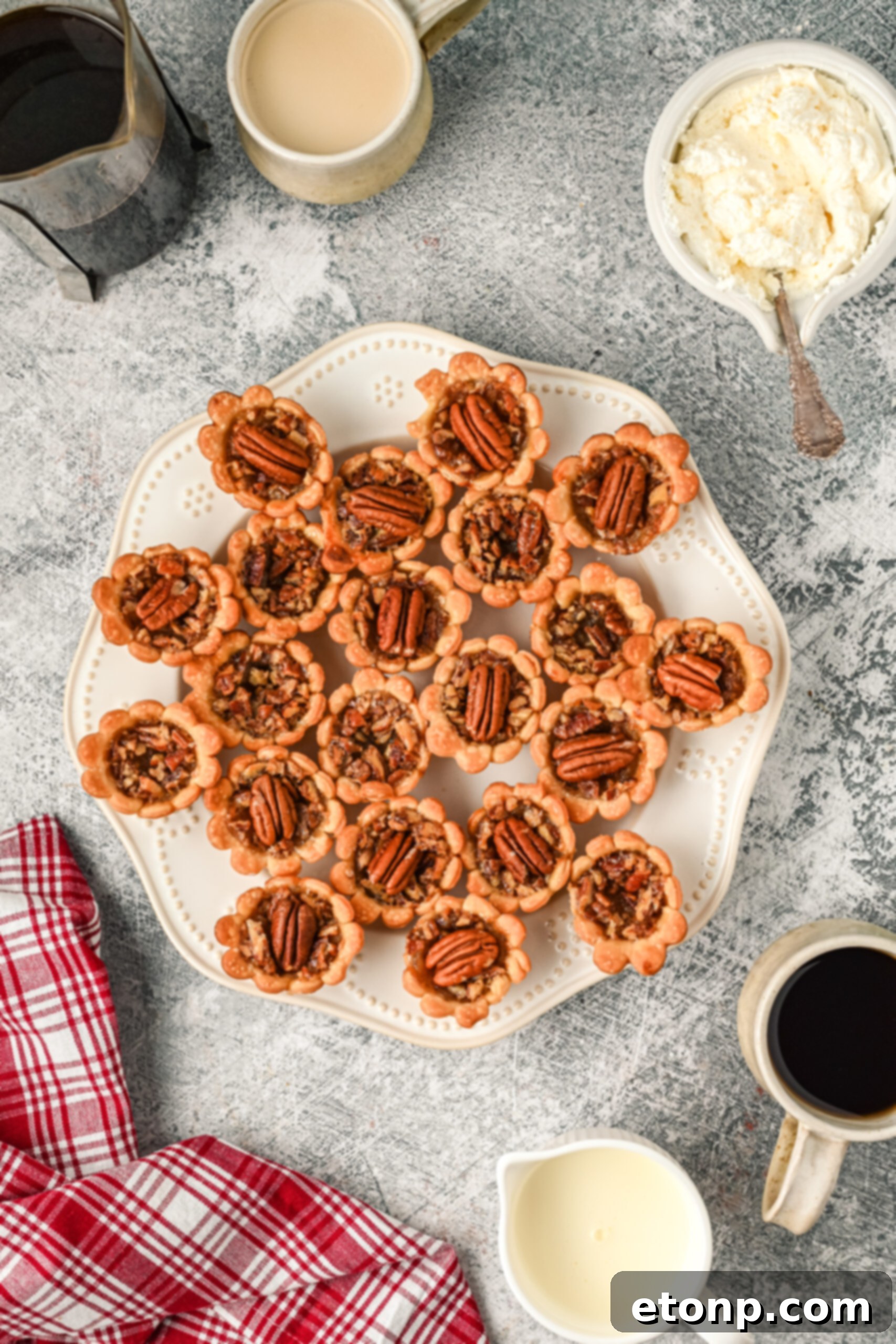 Overhead view of perfectly baked mini pecan pies, showcasing their golden crusts and glossy pecan tops on a white serving tray.