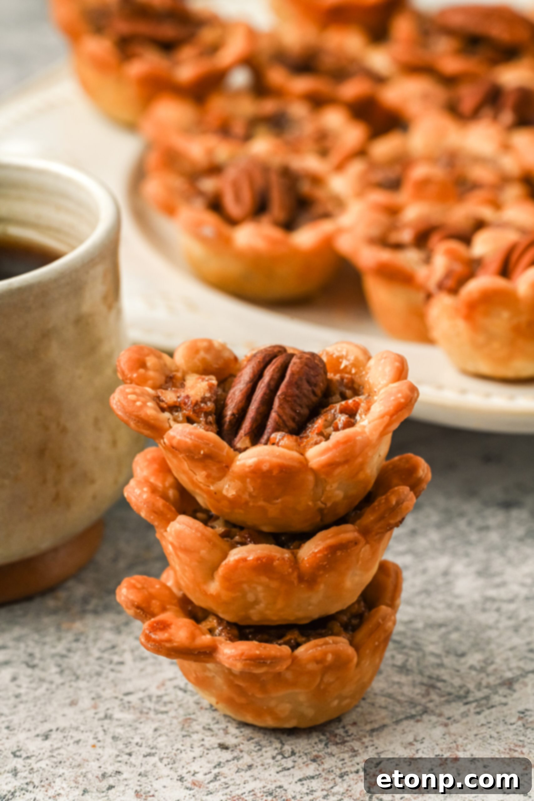 Three perfectly golden mini pecan pies, stacked elegantly to highlight their individual size and inviting texture.