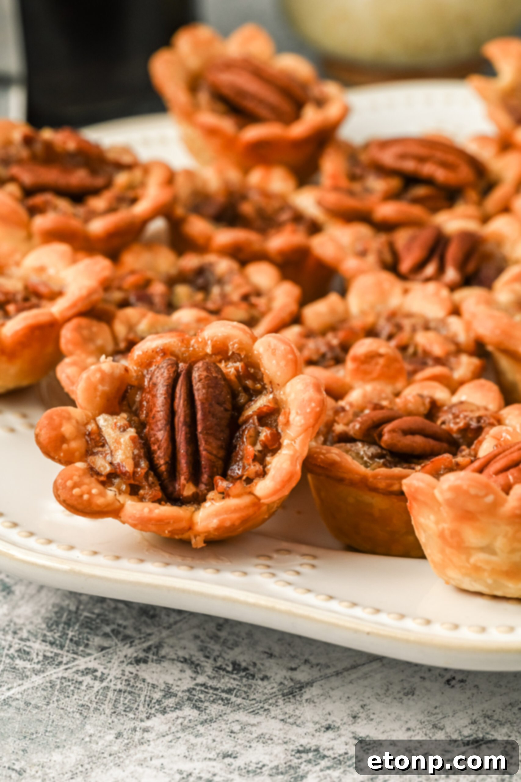 A charming side view of several mini pecan pies, beautifully arranged on a pristine white serving tray, ready to be enjoyed.